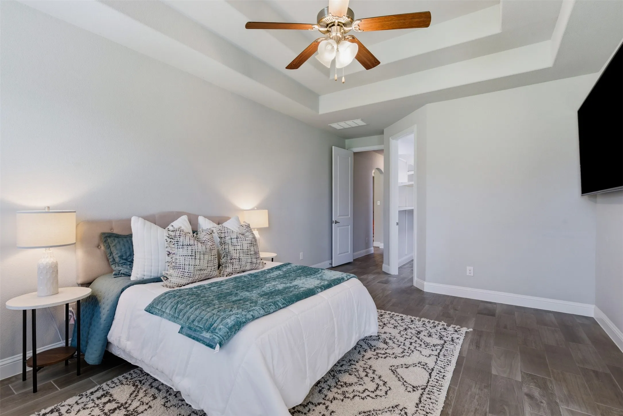 Recessed tray ceiling with a ceiling fan, wood-finish flooring, and white baseboards