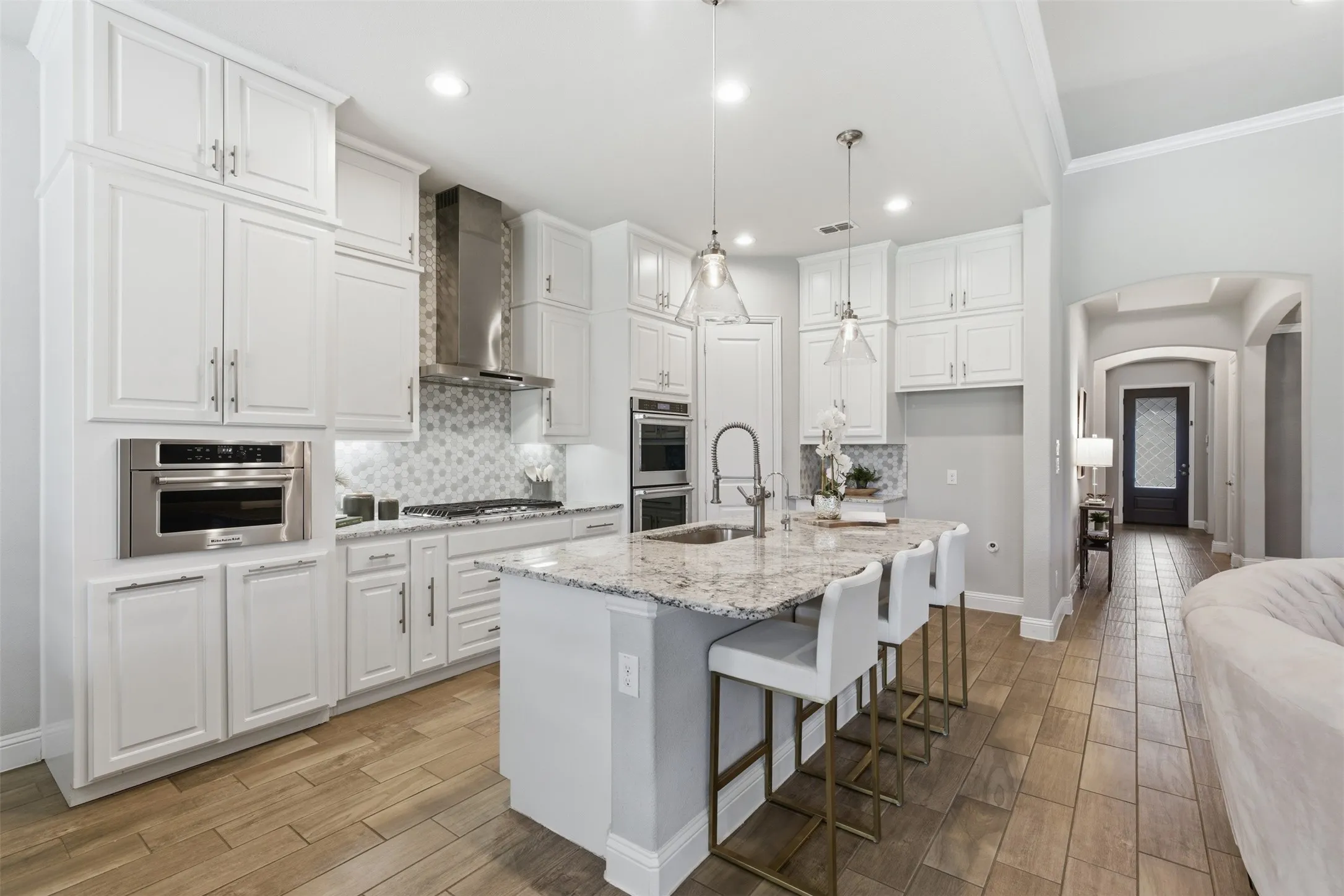 Modern kitchen featuring an expansive center island with seating, white shaker cabinetry, stainless steel appliances, and wood-finish tile flooring
