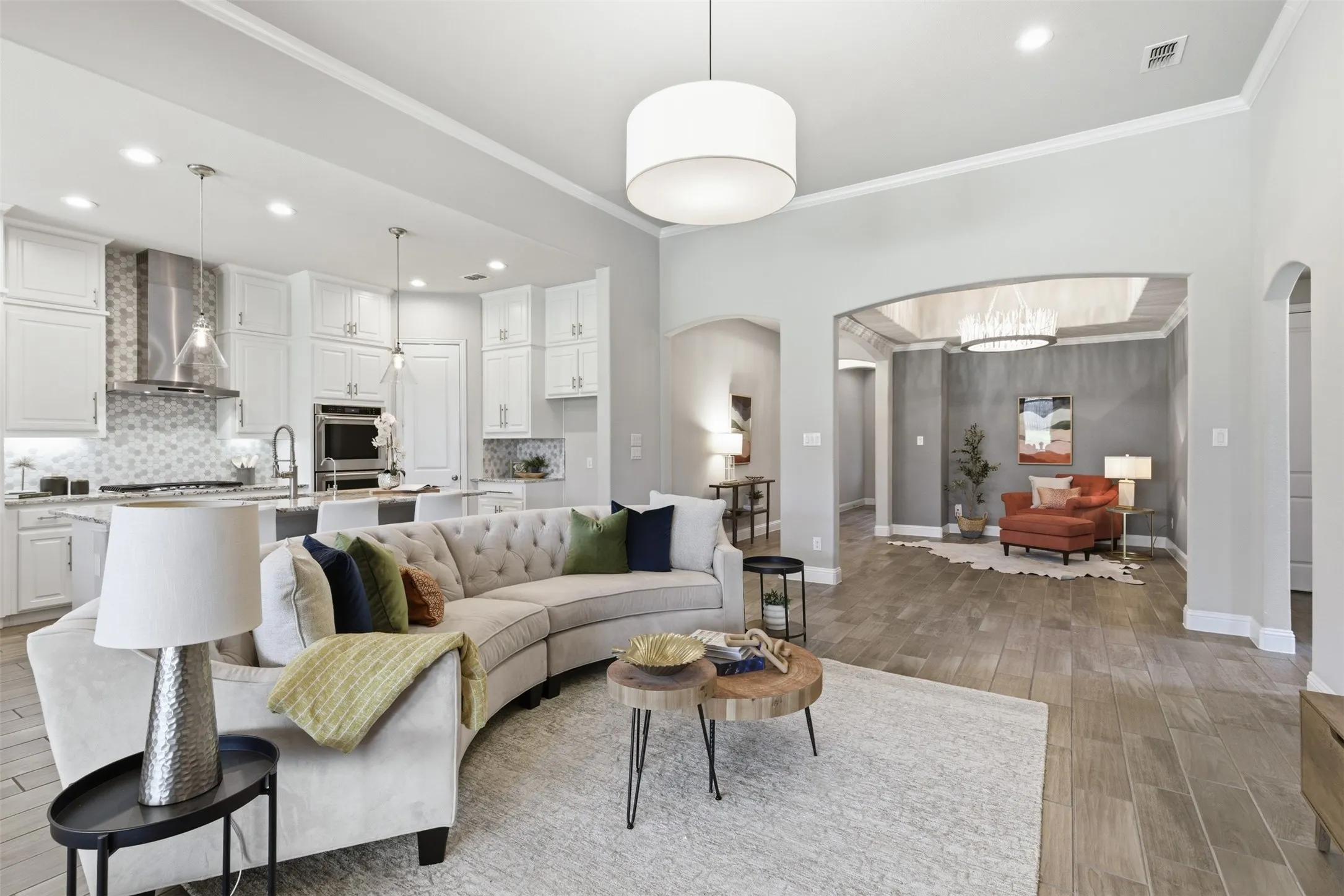 Open-concept living space with wood-finish flooring, a white kitchen, and an arched entryway