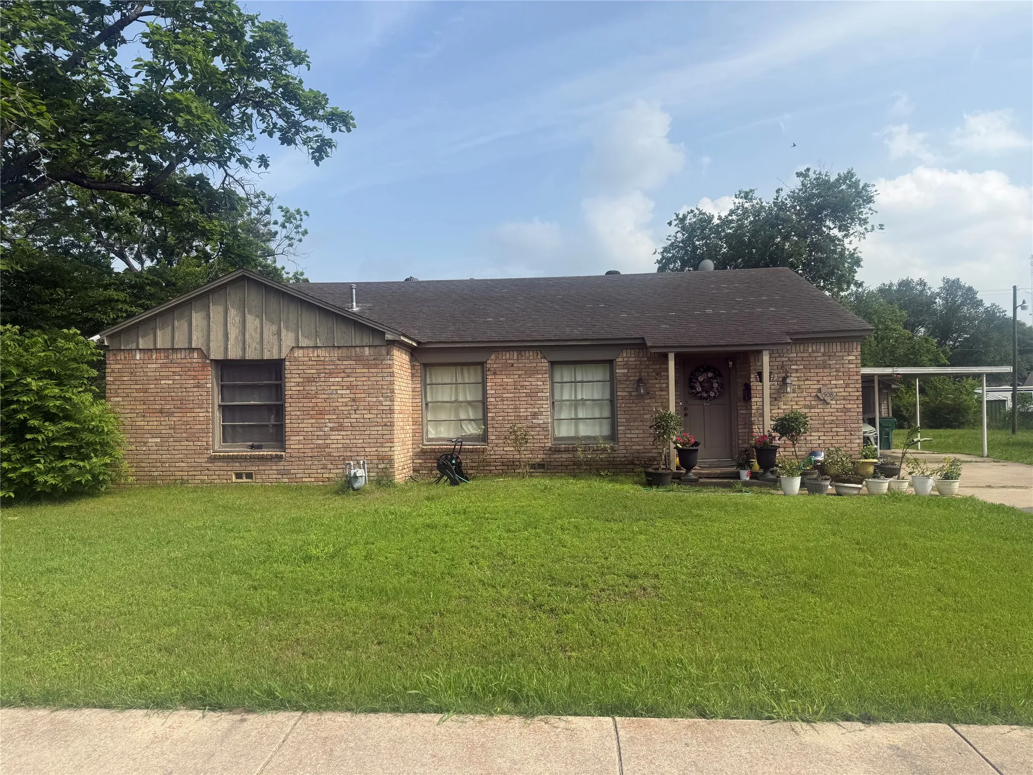 Brick facade home featuring a covered front porch, an attached carport, and a dark shingle roof