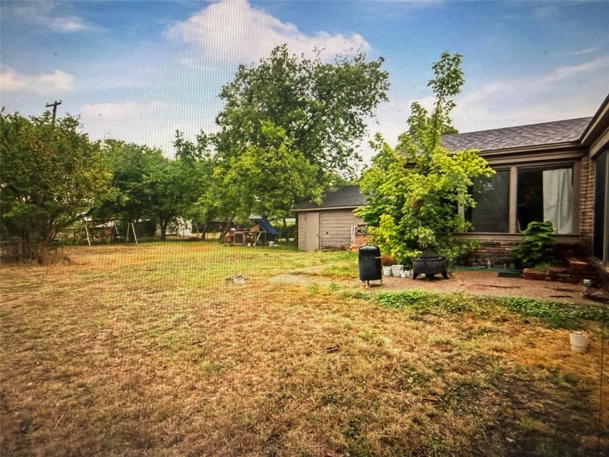 Expansive backyard featuring mature trees, a detached storage shed, and a privacy fence