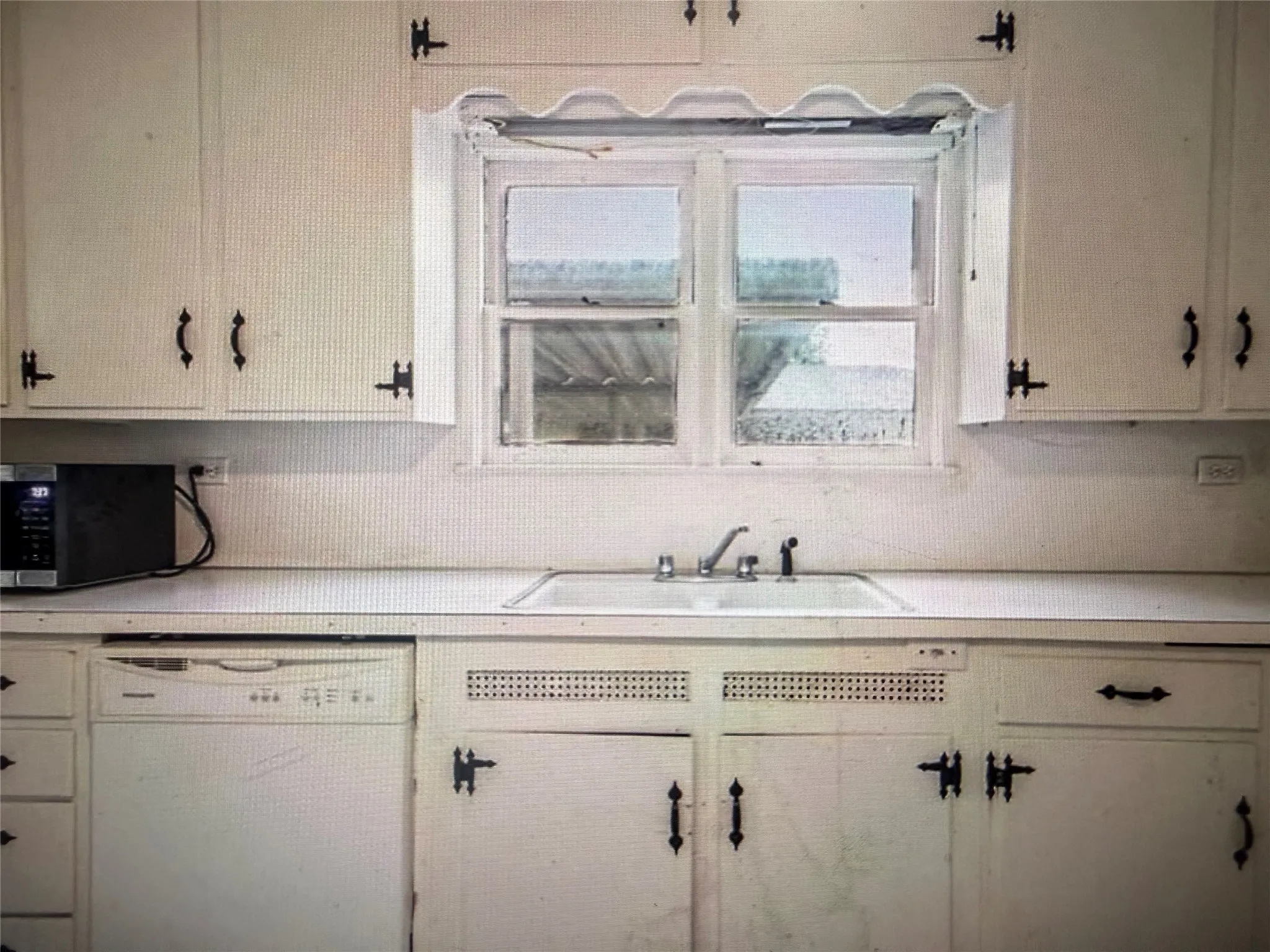 Kitchen area featuring white cabinetry with black hardware, a window above the sink, and a built-in dishwasher