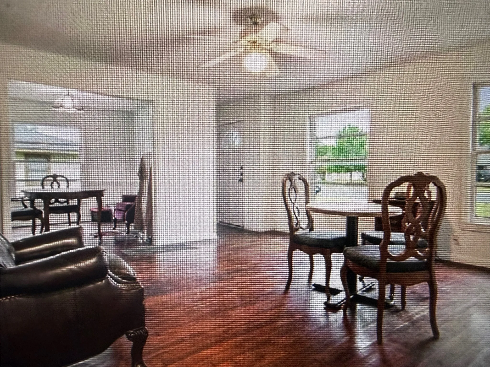 Hardwood-finish flooring throughout, featuring a ceiling fan with integrated lighting, multiple windows providing natural illumination, and a front entry door with a decorative glass insert