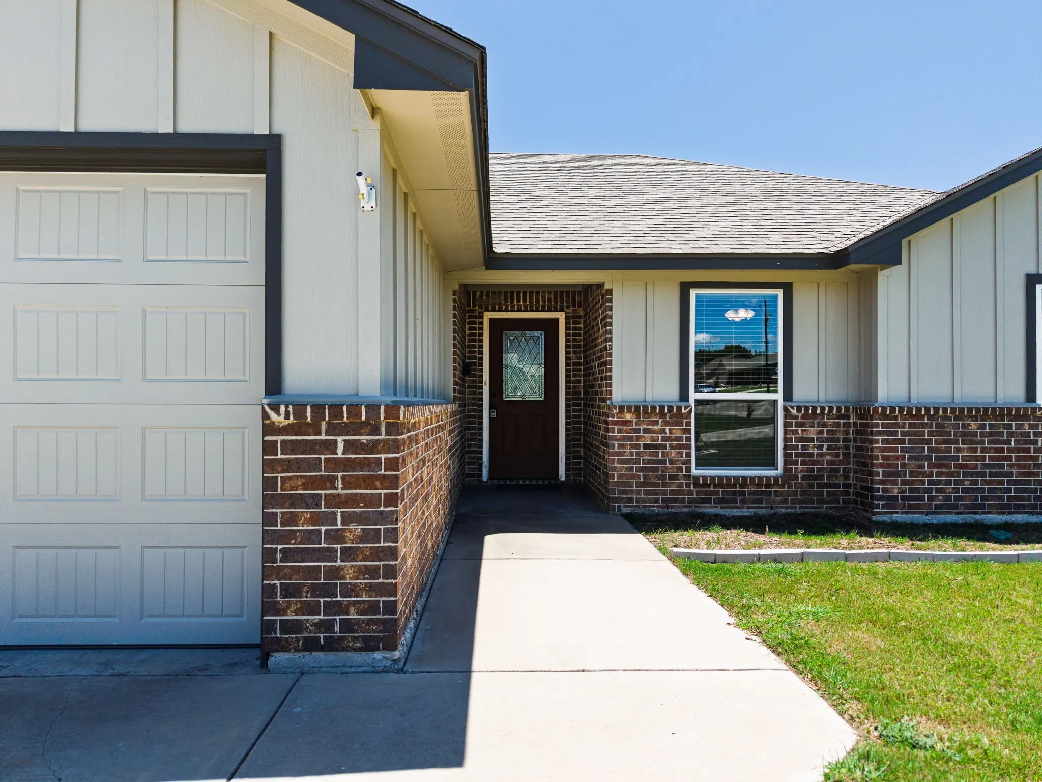 Exterior featuring brick and vertical siding, a paved walkway, and an attached garage with a panel door