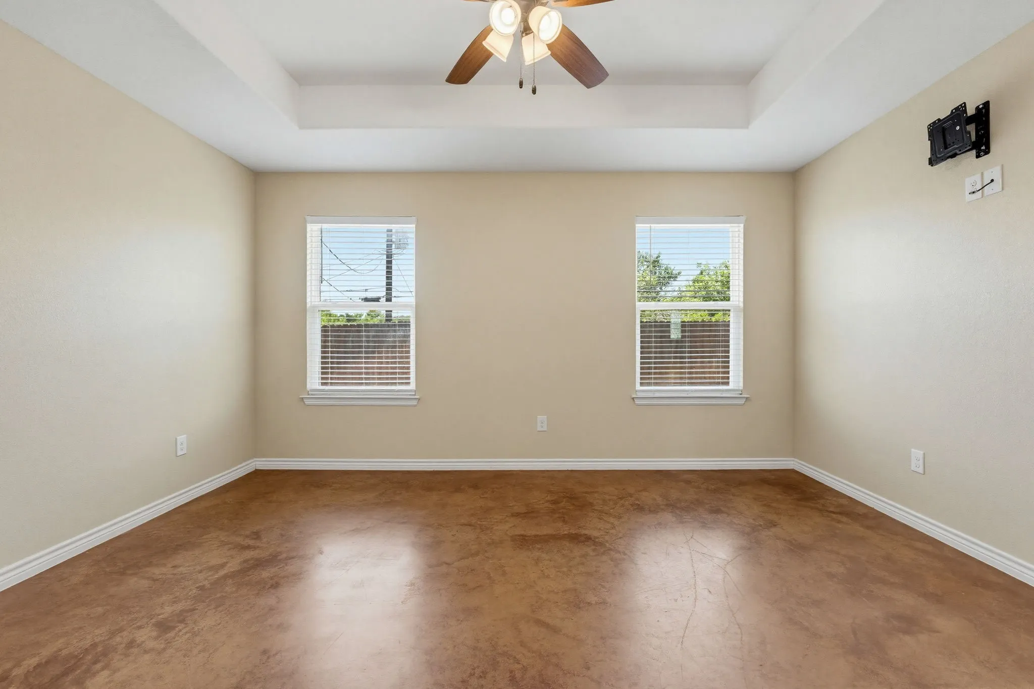 Room featuring a tray ceiling with a ceiling fan, two windows with blinds, and stained concrete flooring