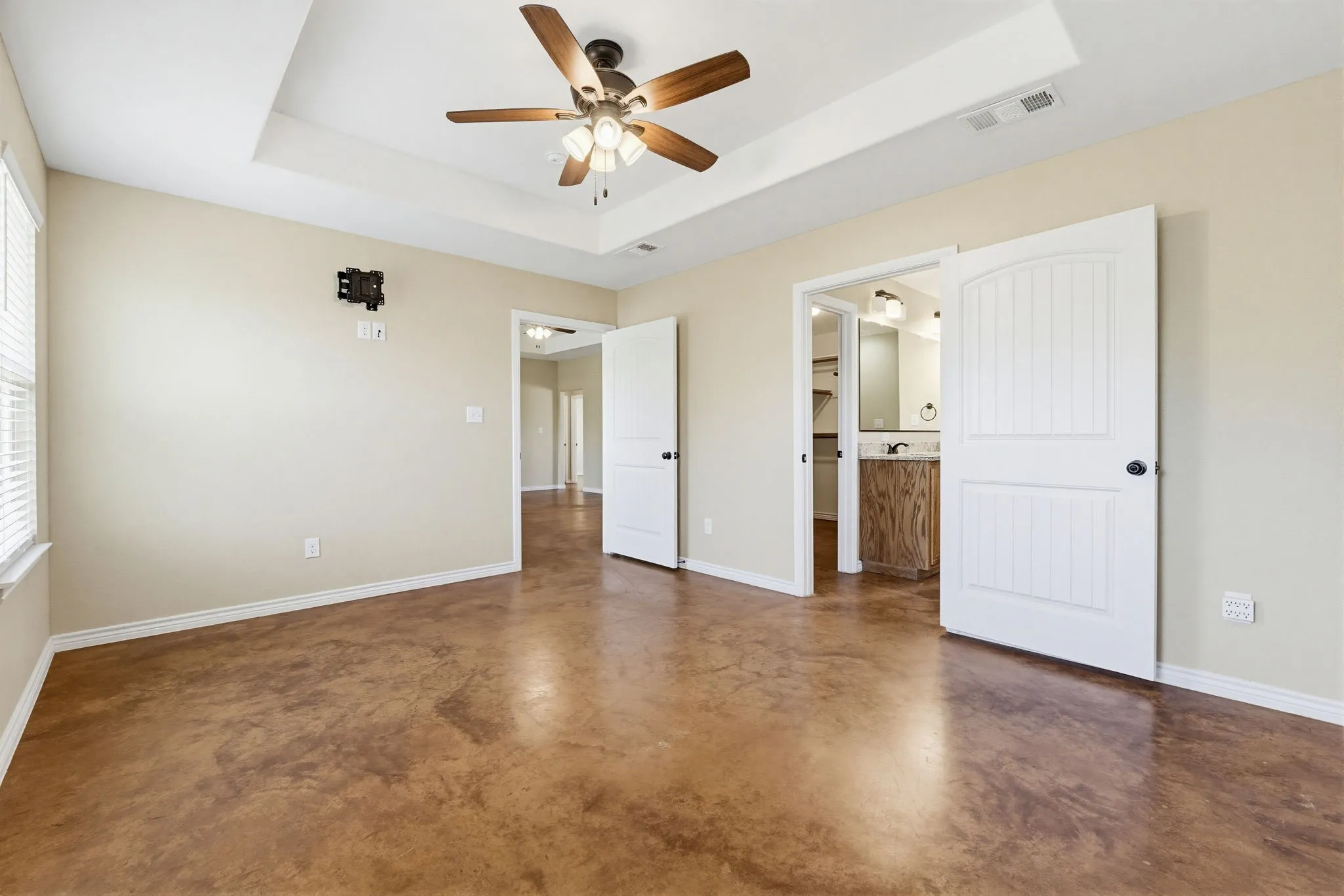 Spacious room featuring tray ceiling, ceiling fan, and stained concrete flooring