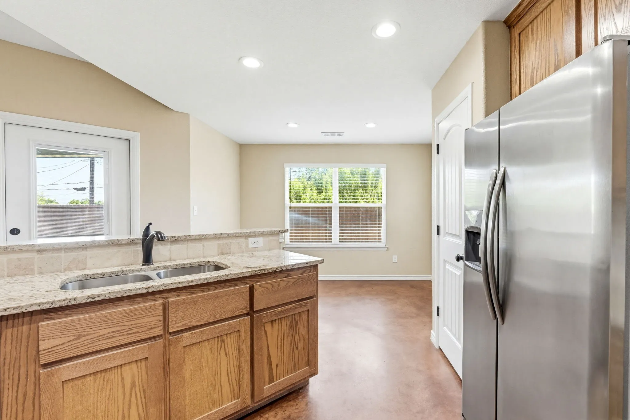 Kitchen island featuring a double basin stainless steel sink with a matte black faucet, granite countertops, and a tile backsplash