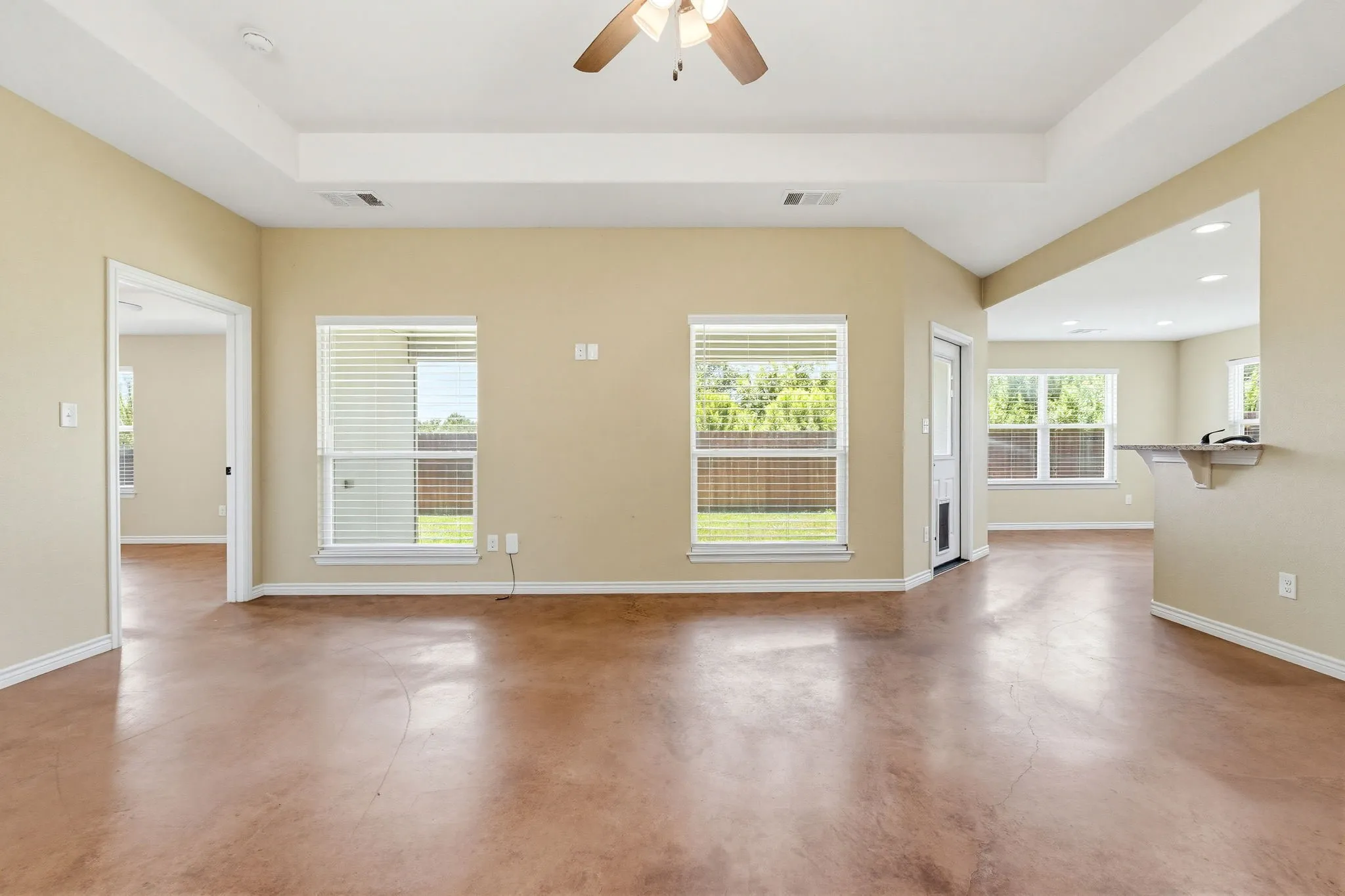 Spacious living area featuring a tray ceiling, ceiling fan, and stained concrete flooring