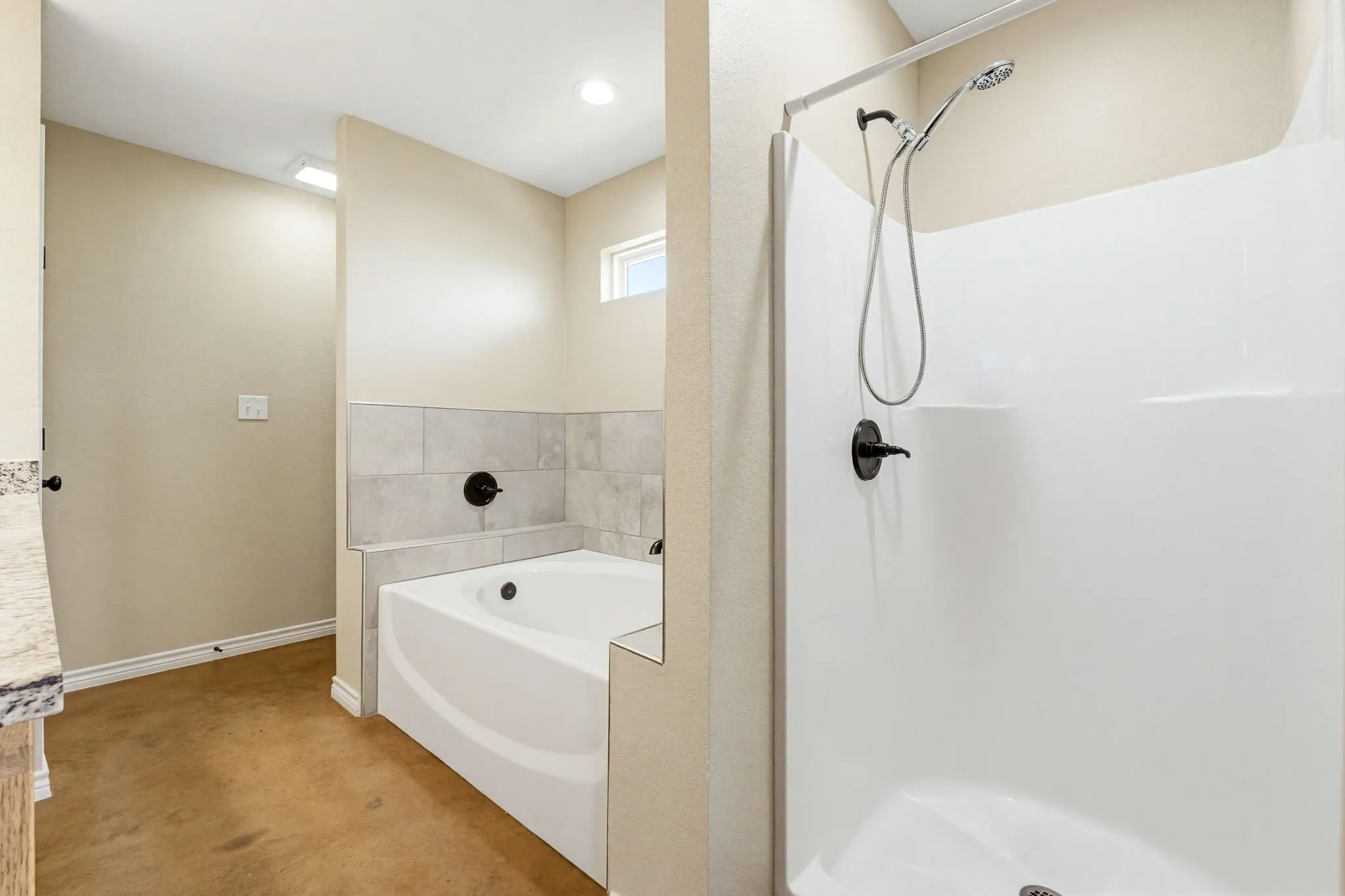 Bathroom featuring a white soaking tub with tiled surround, a separate shower with a handheld fixture, and granite-style countertop