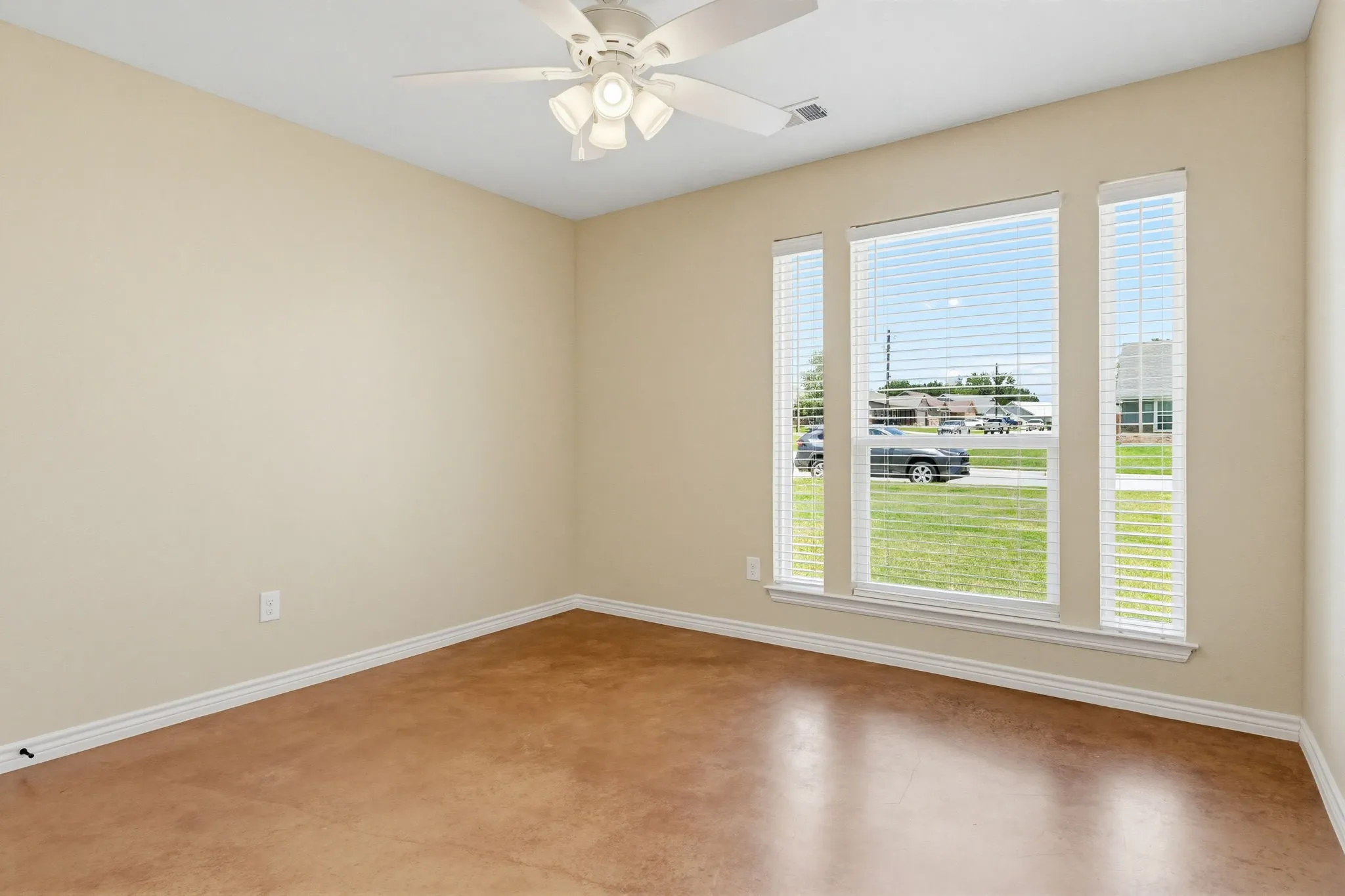 Room featuring a ceiling fan with integrated lighting, three windows with blinds, light-toned wall paint, and sealed concrete flooring