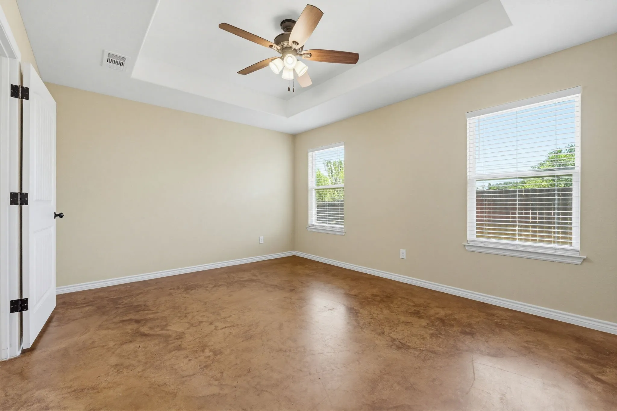 Spacious room featuring a tray ceiling with a ceiling fan, two windows with blinds, light-toned wall paint, white baseboards, and wood-finish flooring