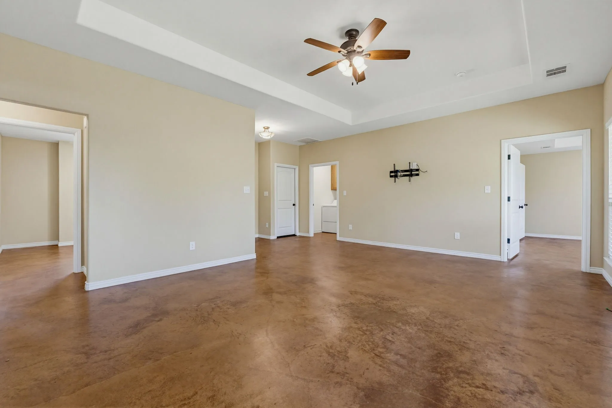 Spacious room featuring rich brown stained concrete flooring, light neutral wall paint, and white baseboards