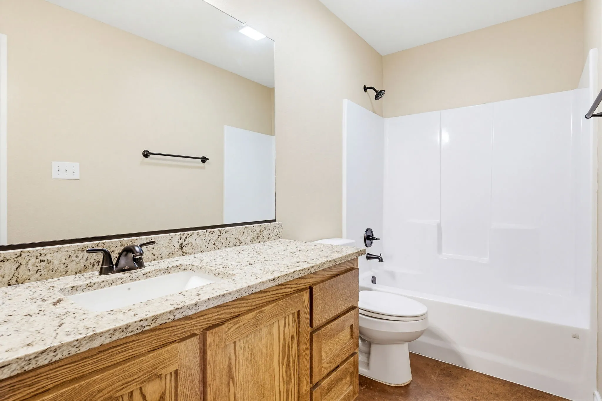 Bathroom featuring a wood-finish vanity with a granite-style countertop, undermount sink, and dark bronze fixtures