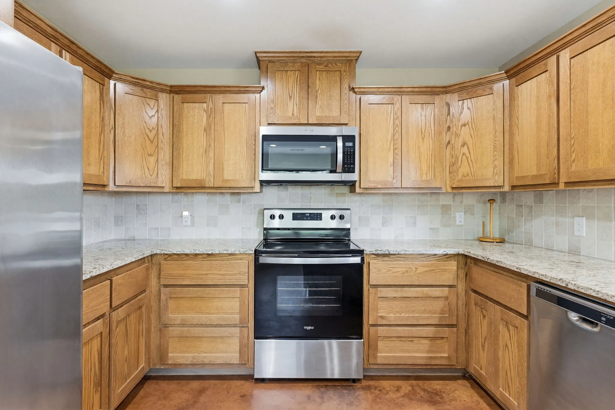 U-shaped kitchen featuring light wood cabinetry with crown molding, granite-style countertops, and a tiled backsplash