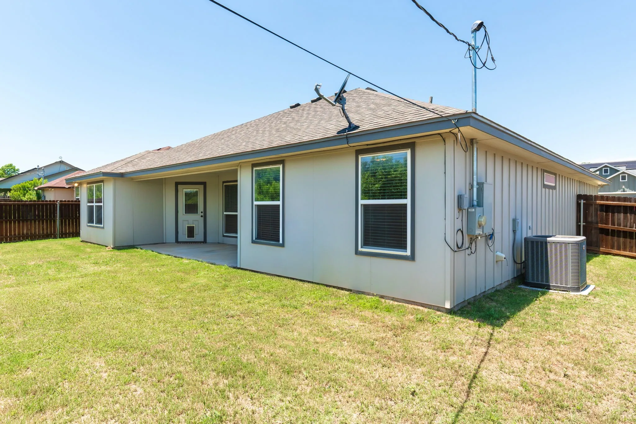 Rear exterior featuring a covered patio, multiple windows with blinds, and a fenced backyard with a manicured lawn