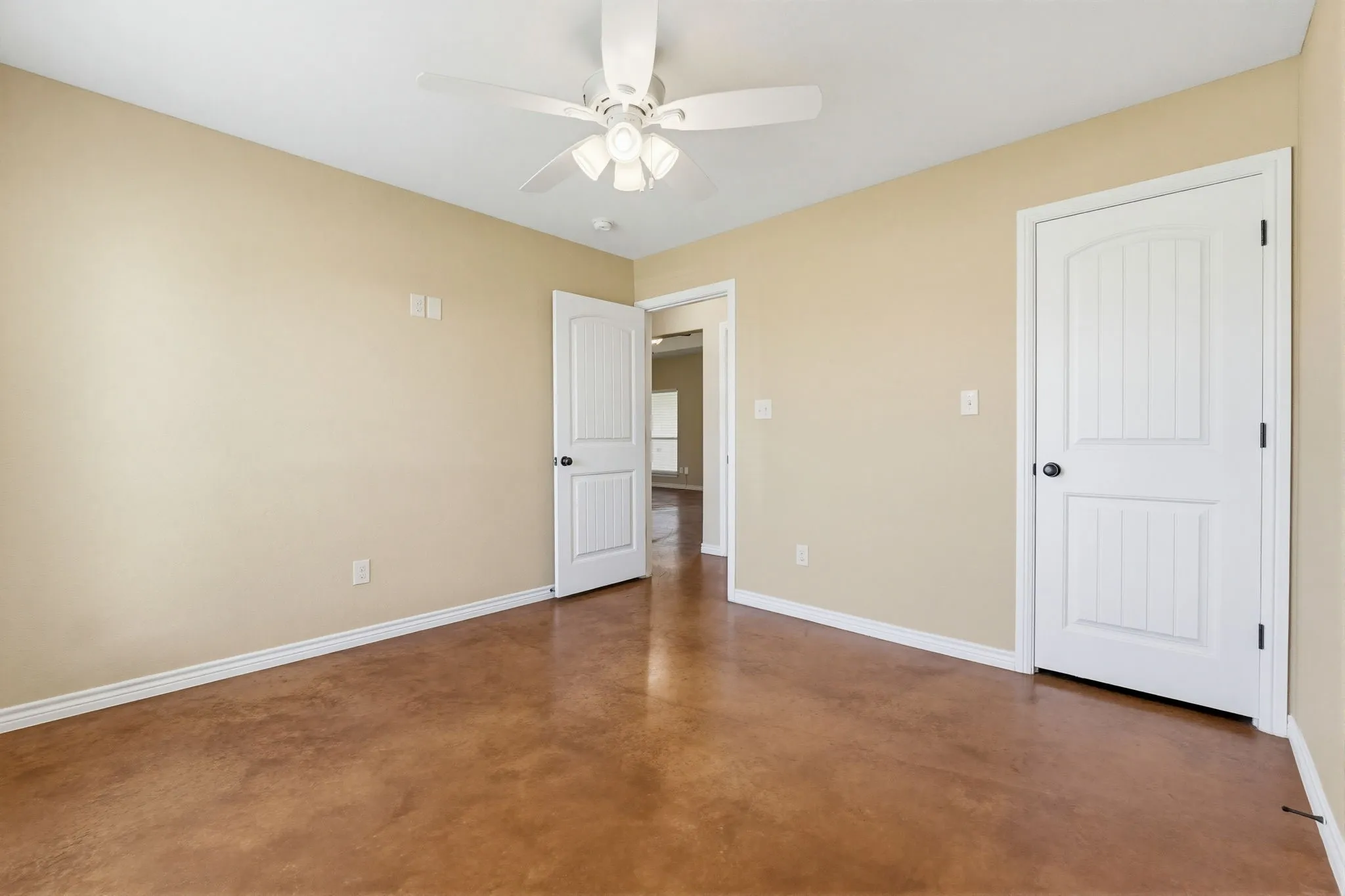 Interior room featuring a ceiling fan, light beige wall paint, white trim, and stained concrete flooring