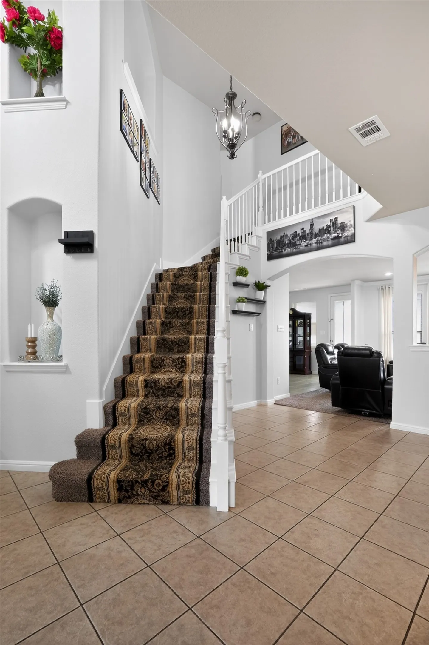 Grand foyer with tile flooring and a carpeted staircase featuring white balusters