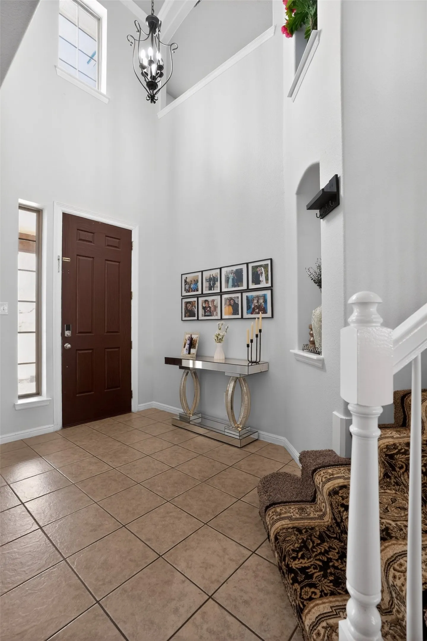 Two-story foyer featuring a dark wood-finish entry door, tile flooring, and a decorative chandelier