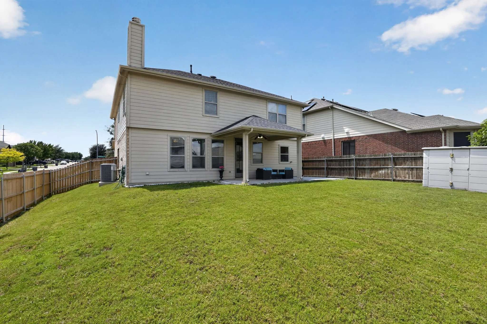Expansive backyard featuring a lush lawn, wood privacy fencing, and a covered patio