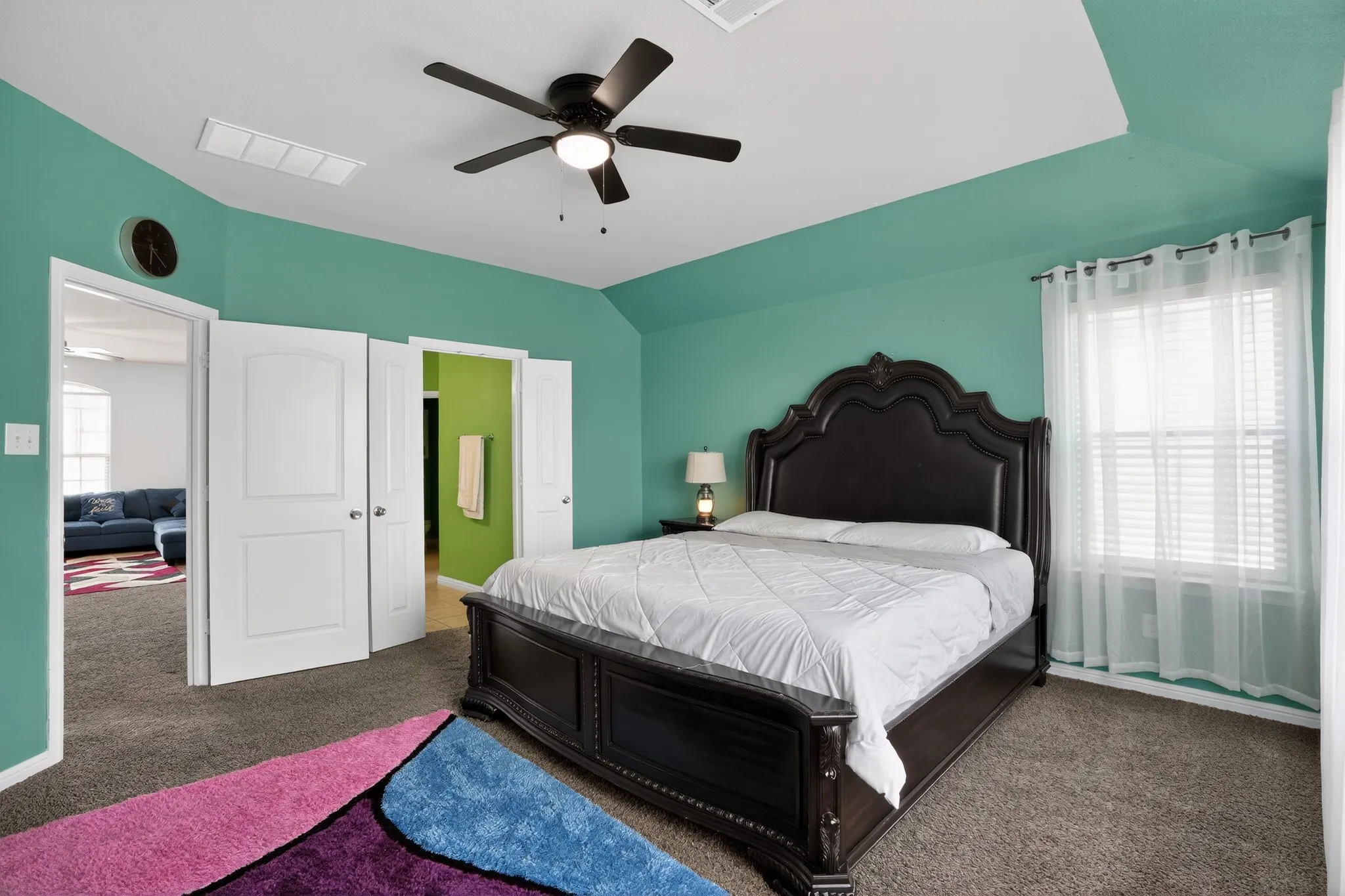 Carpeted room featuring a ceiling fan with integrated lighting, a tray ceiling detail, and a window dressed with sheer white curtains