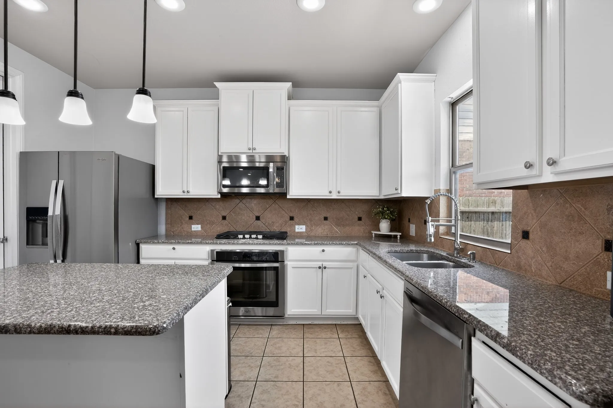 Kitchen featuring a central island with a granite countertop, white cabinetry, stainless steel appliances, a tile backsplash, and tile flooring