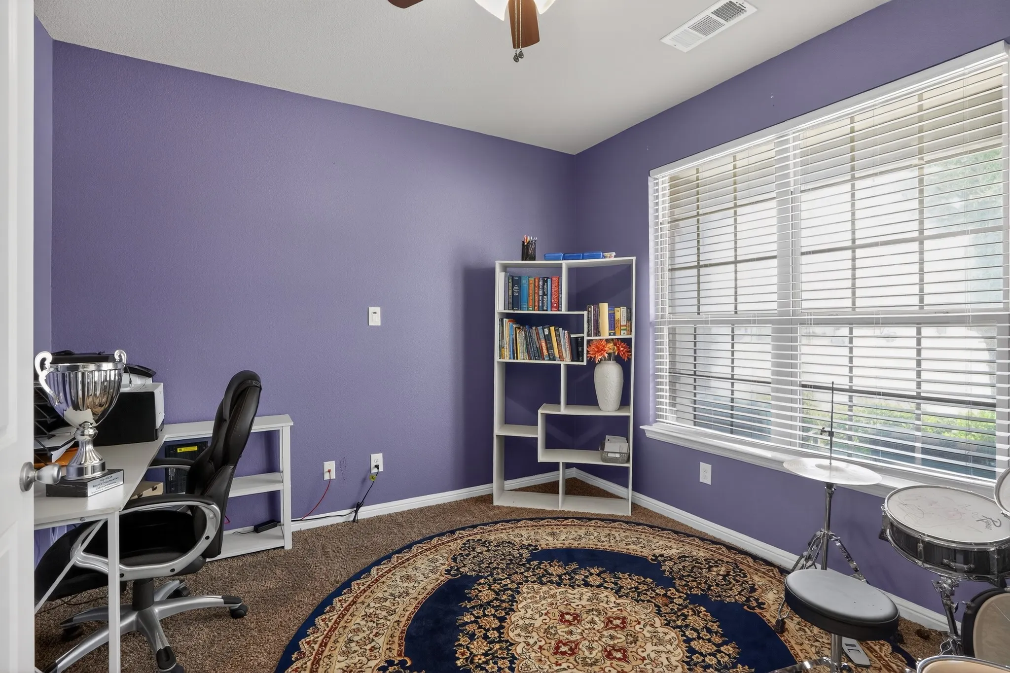 Room featuring a large window with horizontal blinds, a ceiling fan, and carpeted flooring