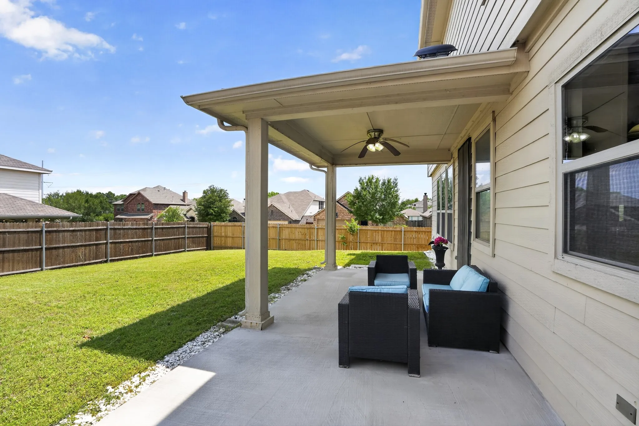 Covered patio featuring a concrete slab, two ceiling fans, and a light beige siding exterior