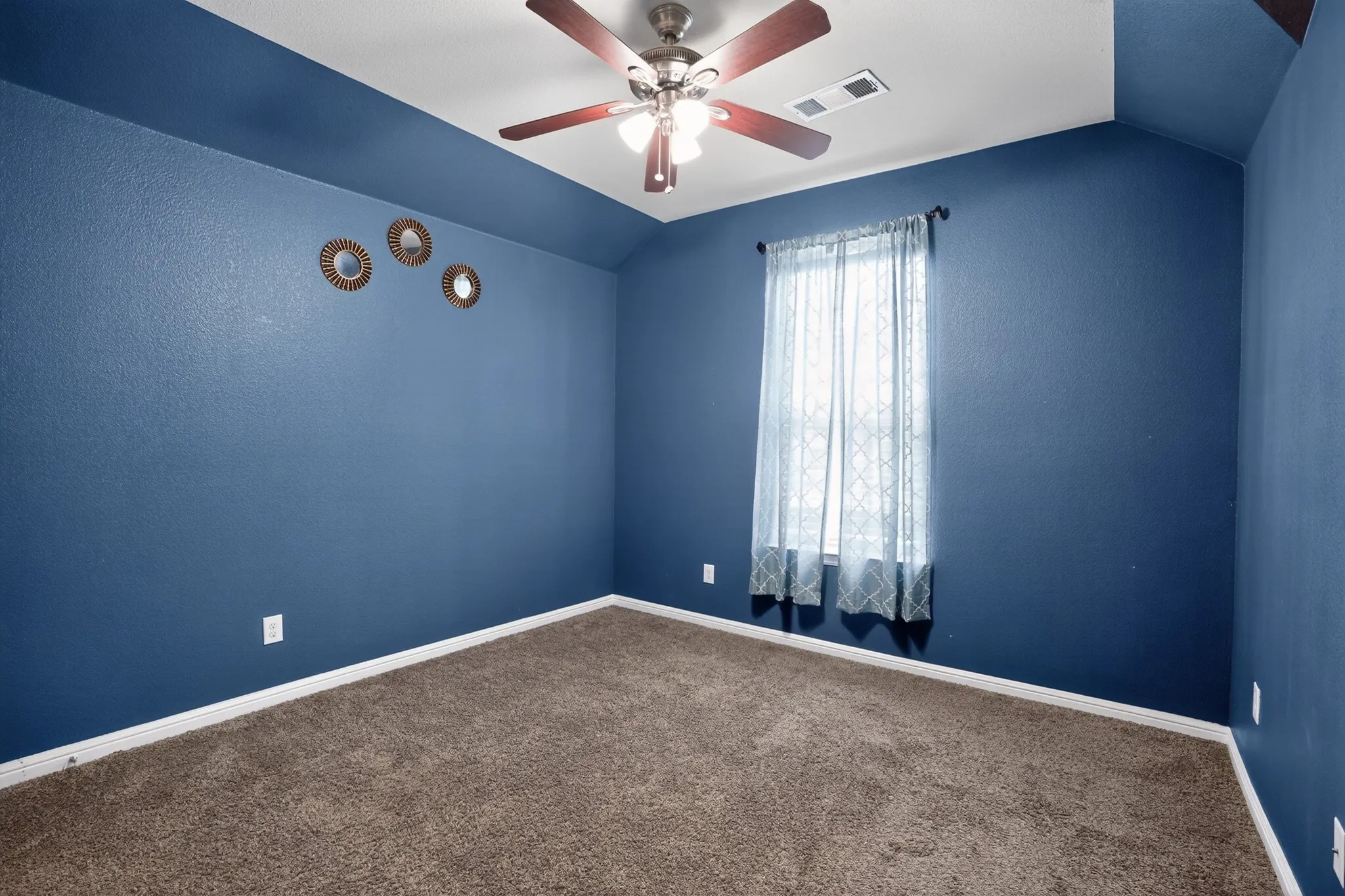 Carpeted room with a vaulted ceiling and a wood-finish ceiling fan with integrated lighting