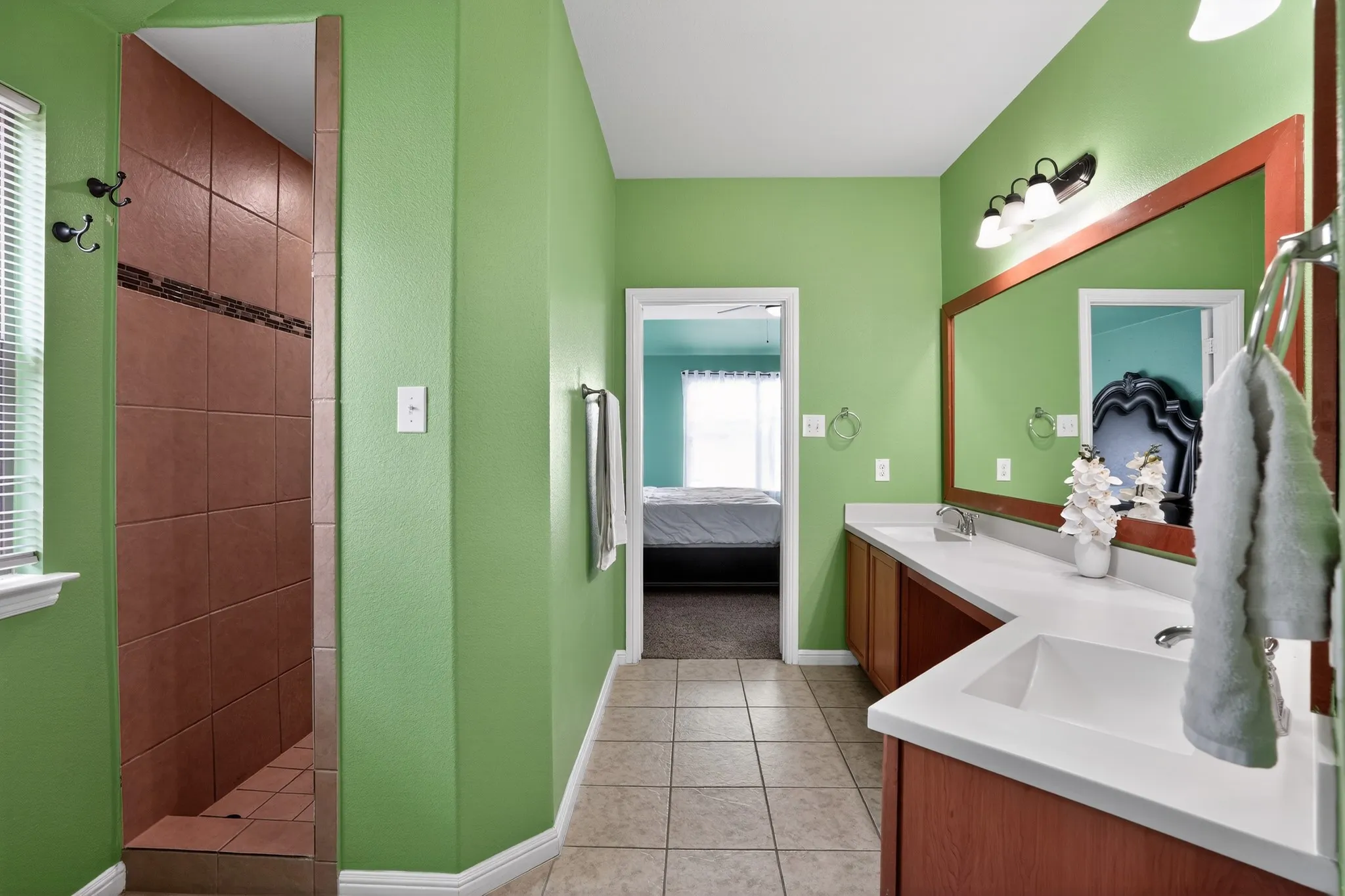 Bathroom featuring a tiled shower stall with a decorative accent band, a double vanity with white countertops, integrated sinks, and wood-finish cabinetry