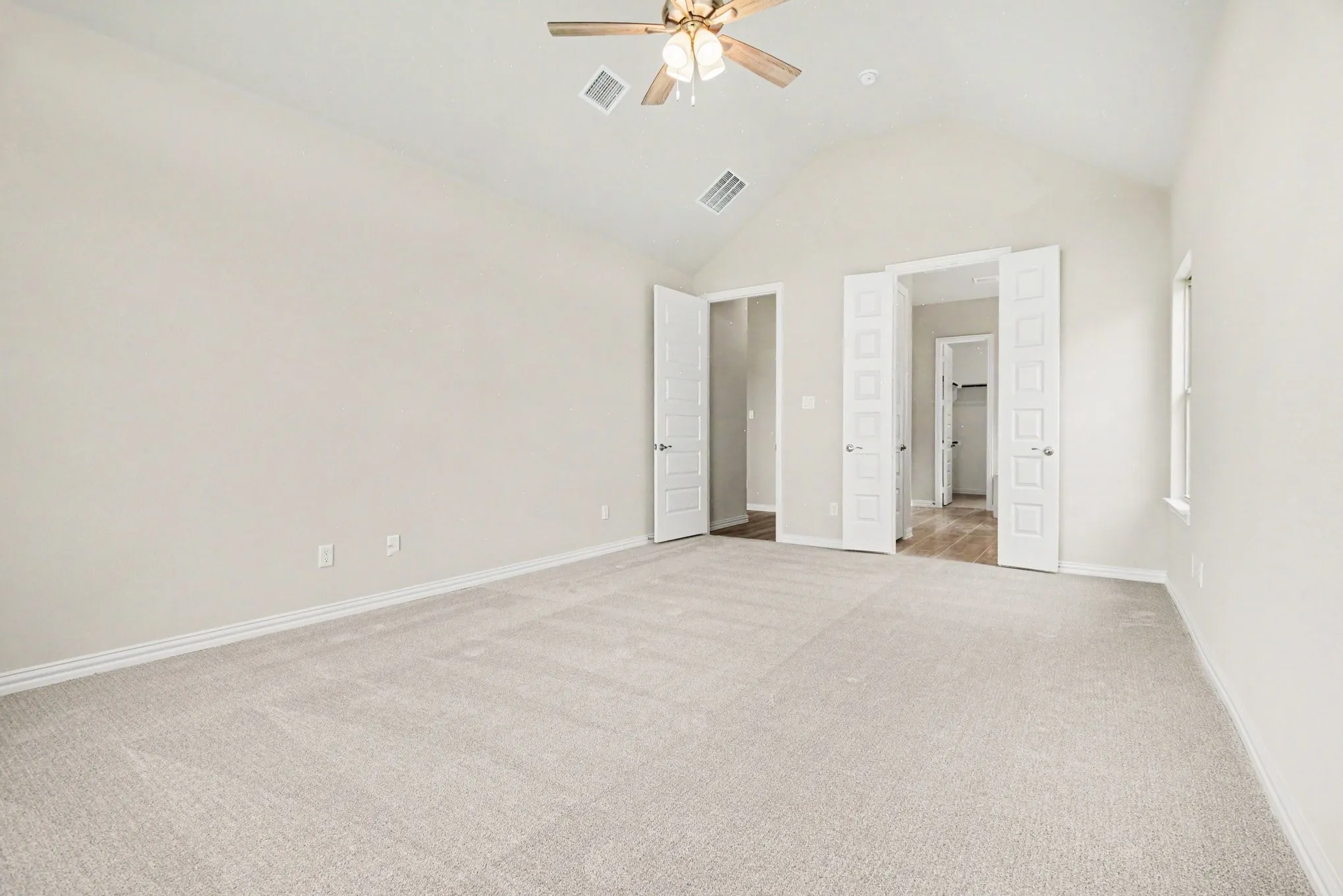 Vaulted ceiling bedroom featuring plush light-toned carpeting, neutral wall finishes, a ceiling fan with integrated lighting, and multiple panel doors