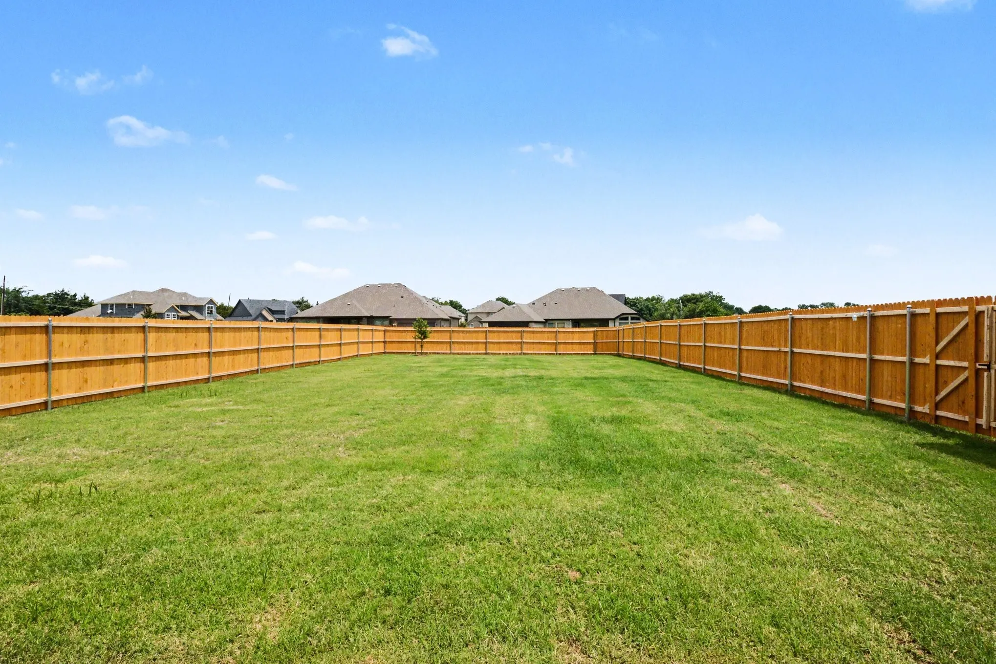 Expansive backyard featuring a manicured lawn, full perimeter wood fencing, and a side gate