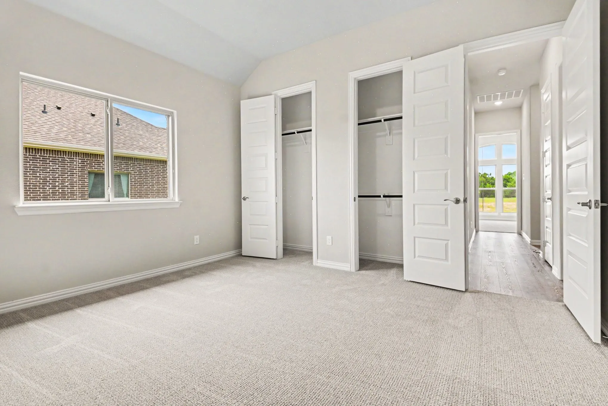 Expansive room featuring light neutral carpeting, a large window, and two built-in closets with bi-fold doors