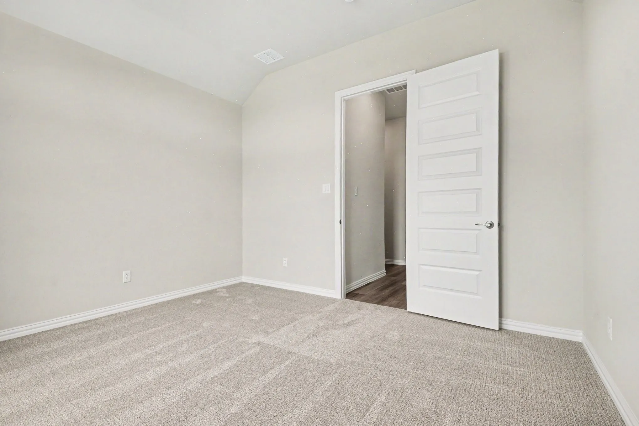 Spacious room featuring light-toned carpeting, neutral wall paint, white baseboards, and a vaulted ceiling