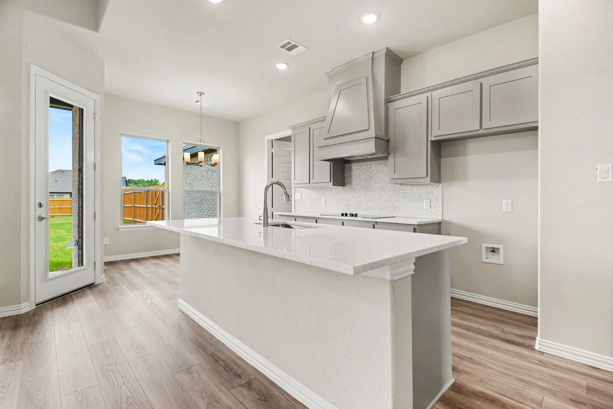 Spacious kitchen featuring a large island with a composite countertop, wood-finish flooring, recessed lighting, and a white tile backsplash