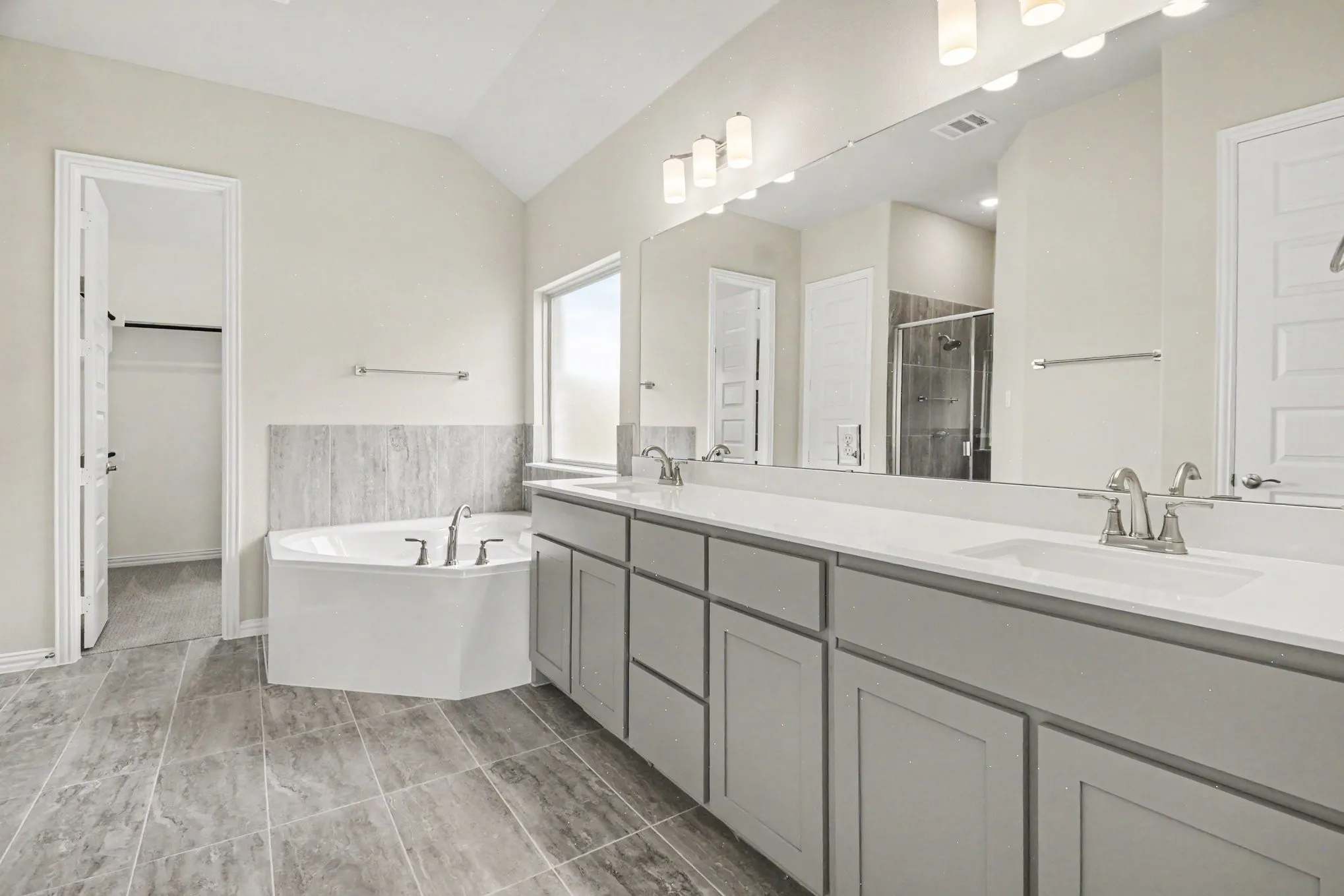 Spacious bathroom featuring a corner soaking tub, dual vanities with white countertops, and expansive mirror