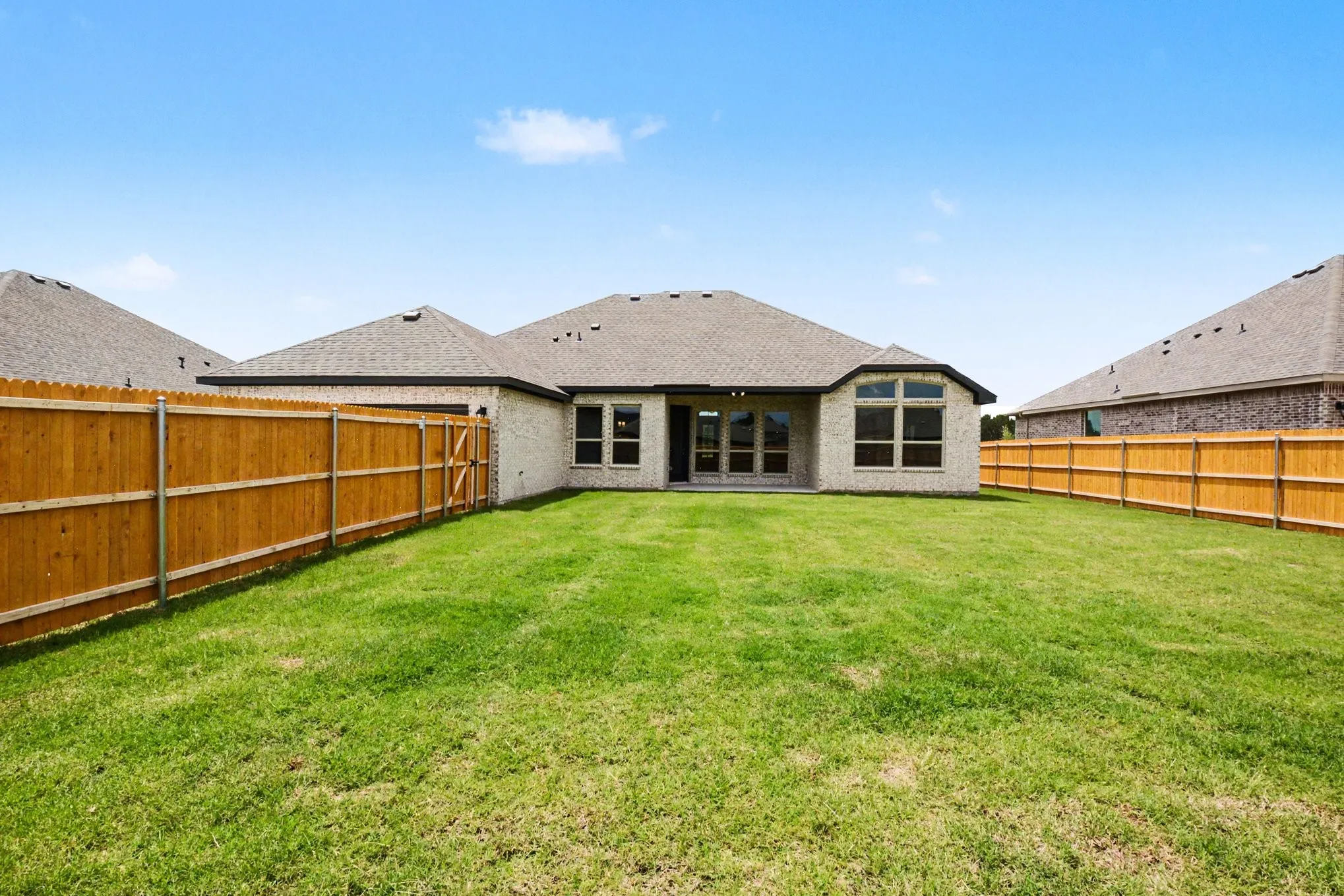 Expansive backyard featuring a manicured lawn, full privacy fencing, light-colored brick exterior, a large bay window, and a patio door