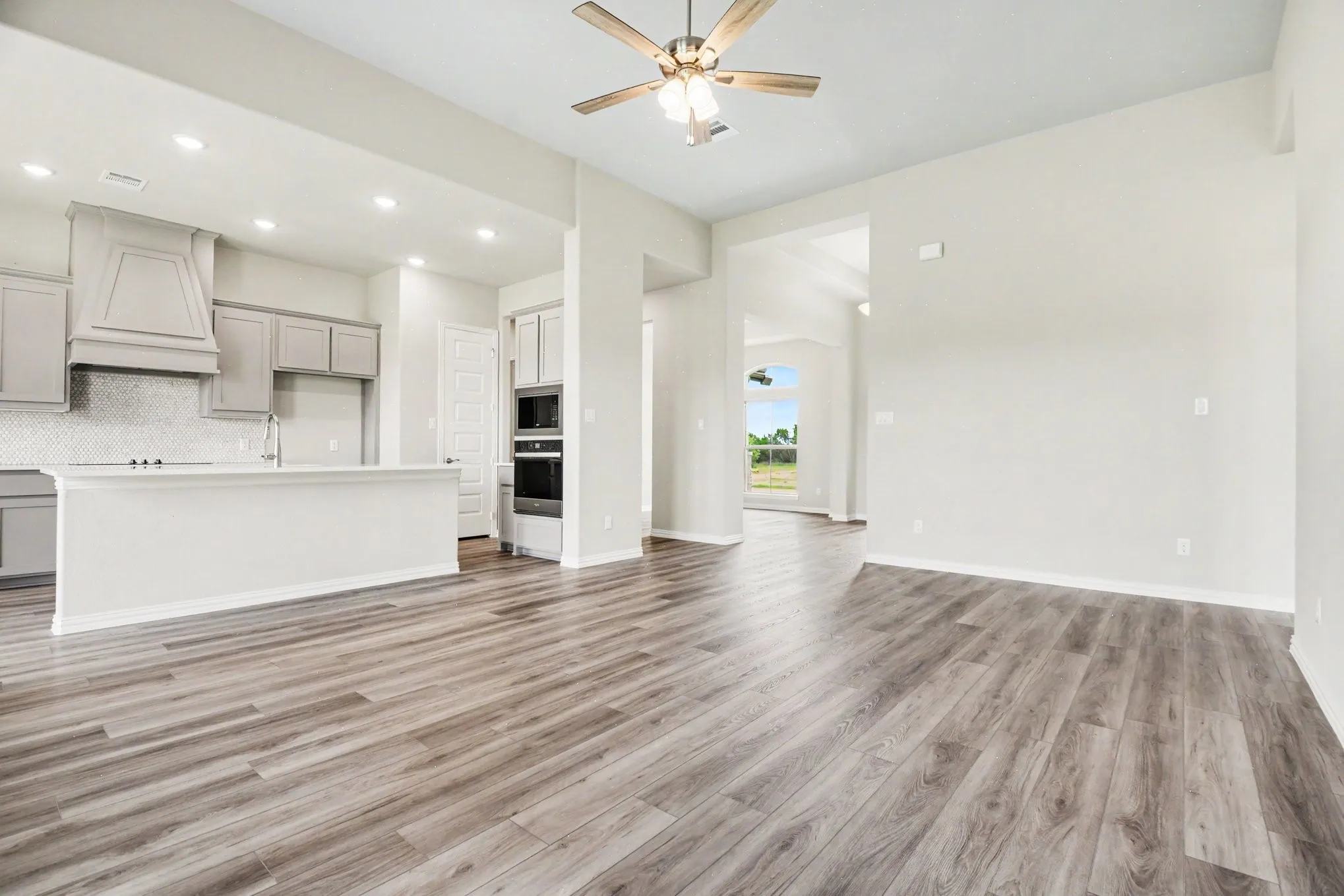 Kitchen and living area featuring wood-finish flooring, recessed lighting, ceiling fan, kitchen island with sink, and built-in double ovens