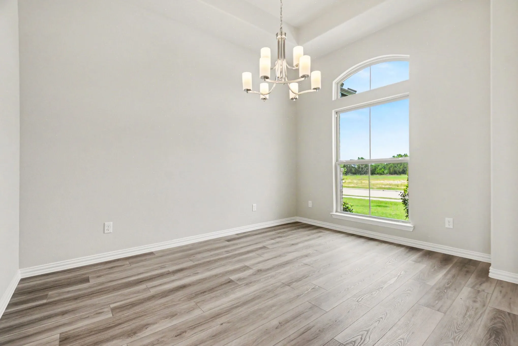 Bright interior space featuring a large arched window, vaulted ceiling, and wood-finish flooring