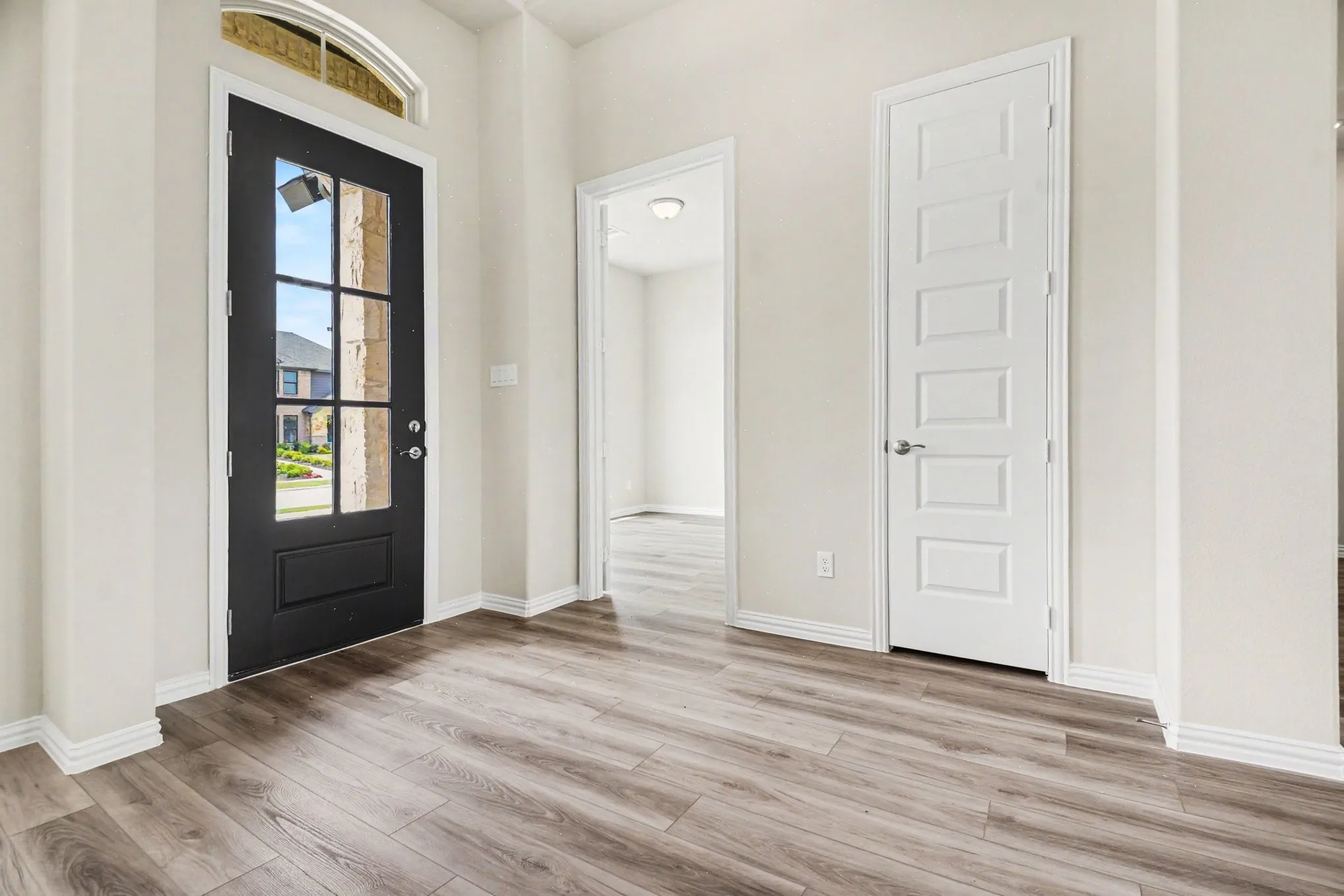 Entryway featuring a black multi-pane glass door with an arched transom window, wood-finish flooring, and crisp white baseboards and trim