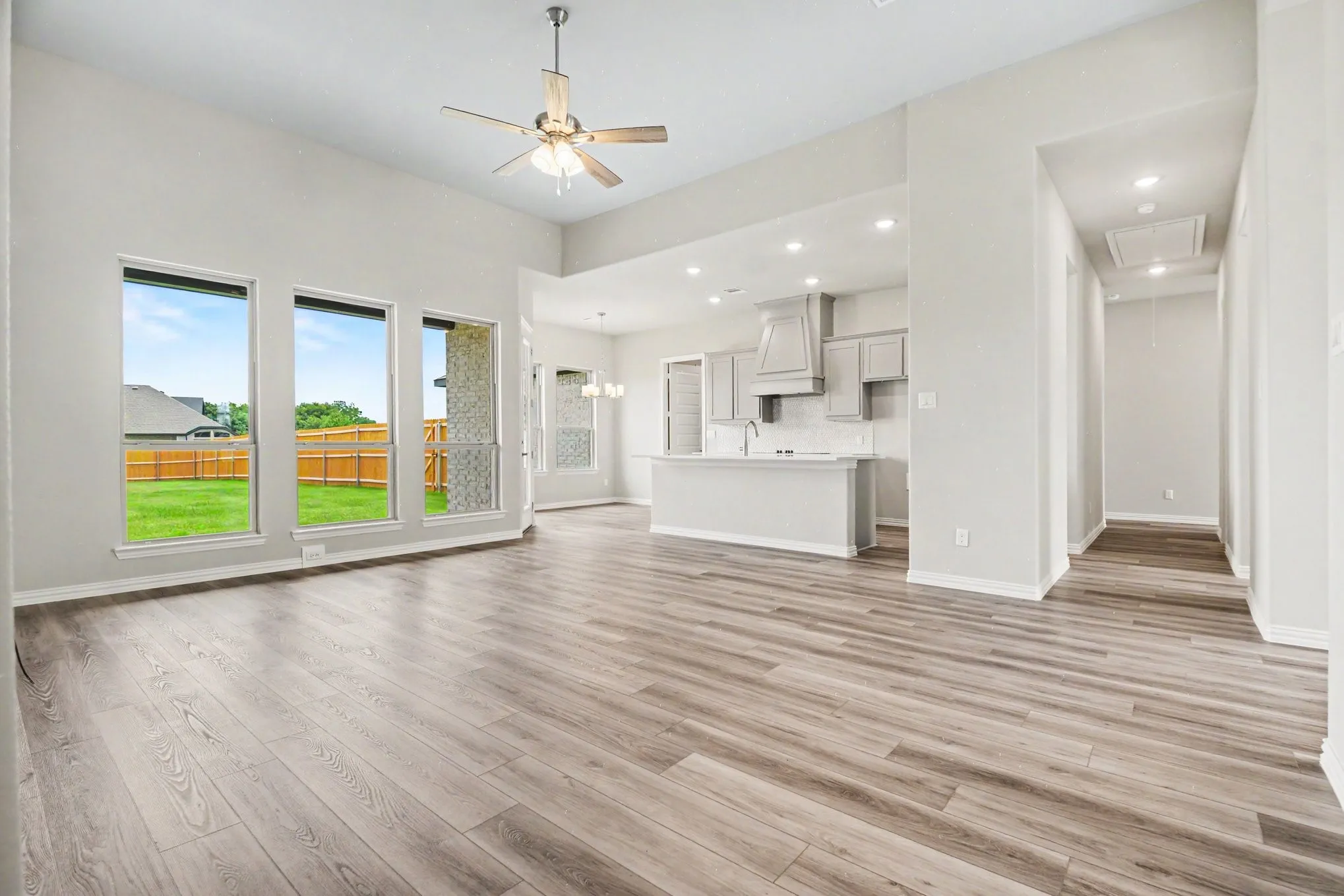 Spacious living area featuring high ceilings, wood-finish flooring, and multiple large windows overlooking a fenced backyard