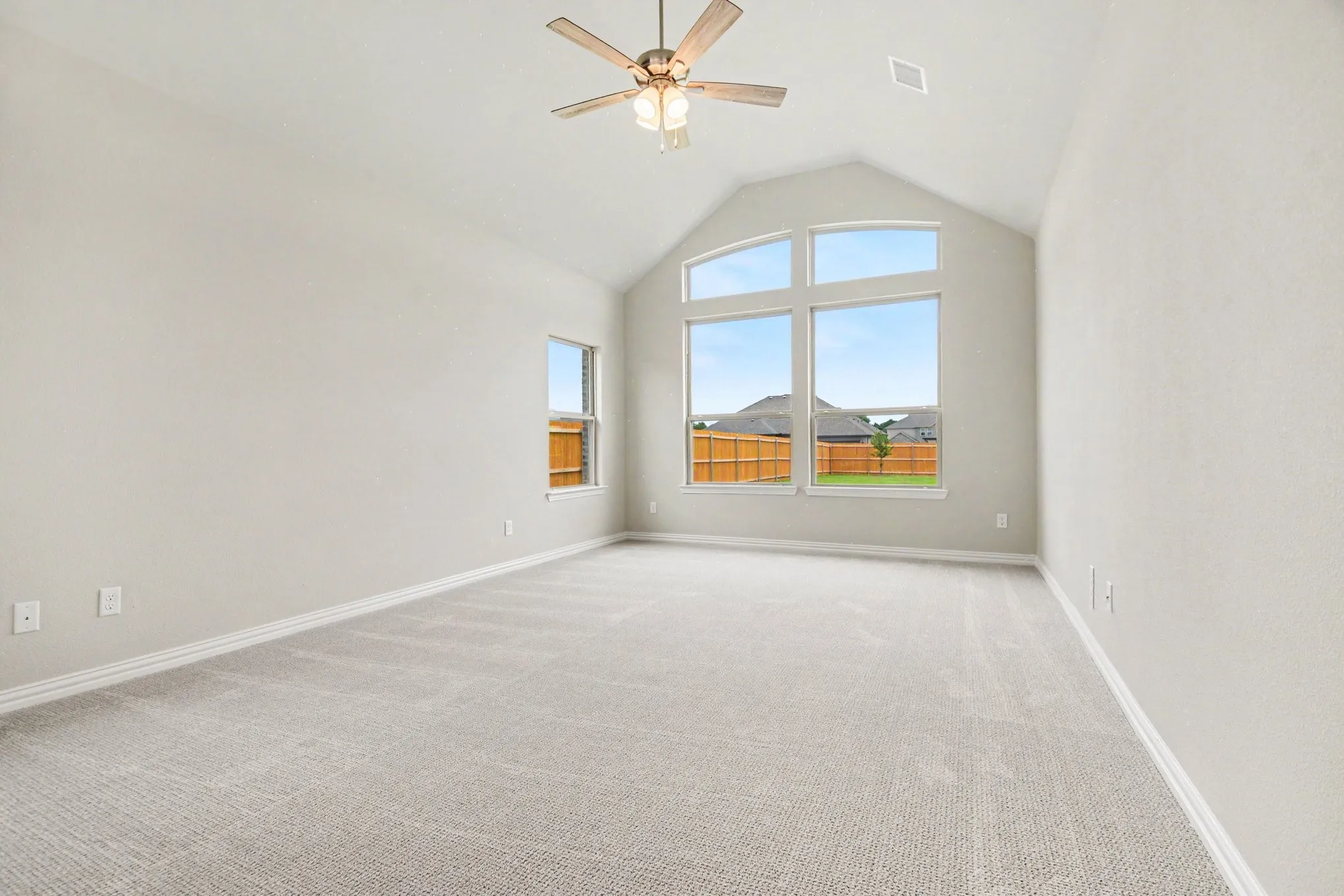 Spacious room featuring vaulted ceilings, light-toned carpeting, a multi-pane arched window, an additional single window, and a ceiling fan with integrated lighting