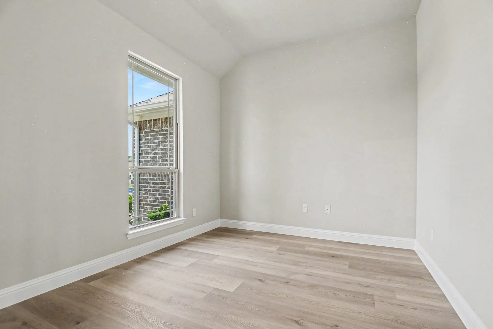 Bright room featuring a single-pane window, vaulted ceiling, and wood-finish flooring