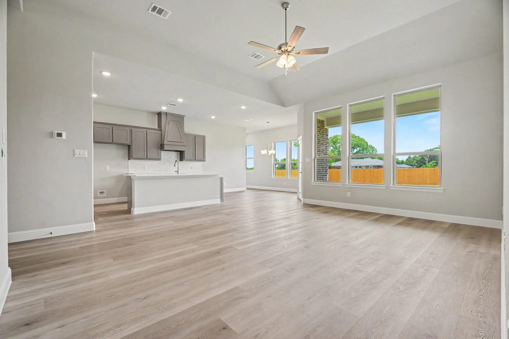 Spacious living area featuring light wood-finish flooring, vaulted ceilings, recessed lighting, and a modern ceiling fan