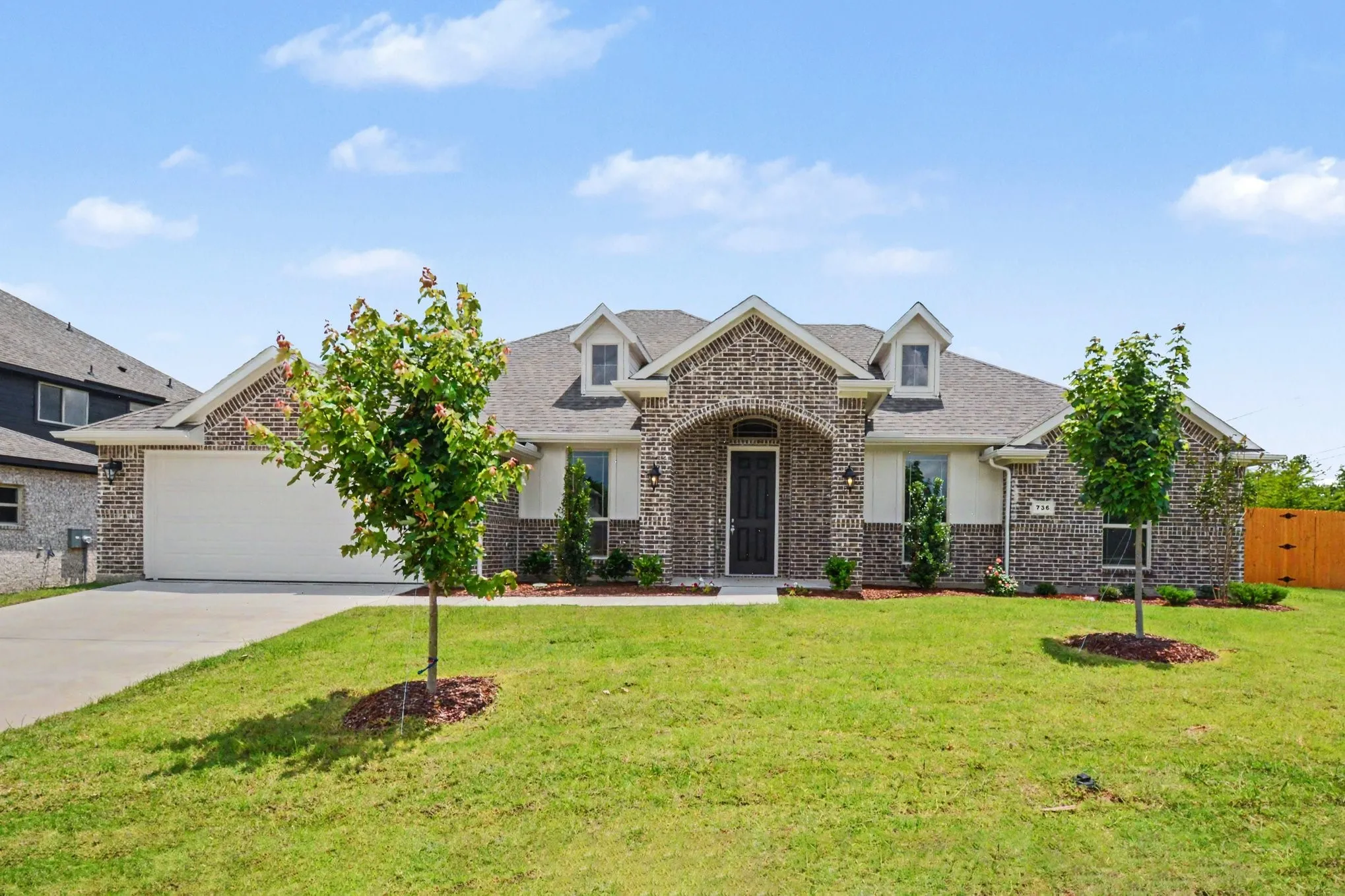 Brick exterior with complementary light siding, an arched entryway, and a two-car garage