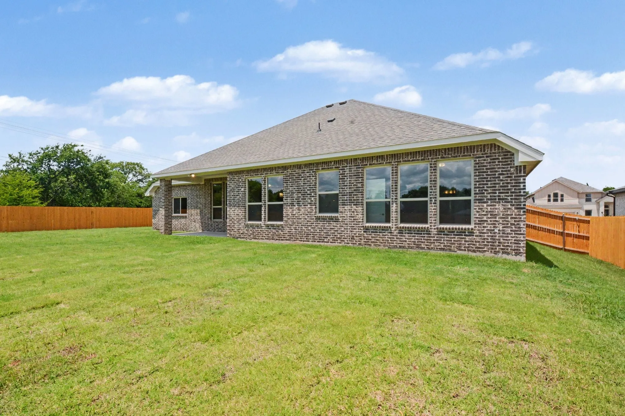 Expansive green lawn with a newly built brick exterior and a privacy fence