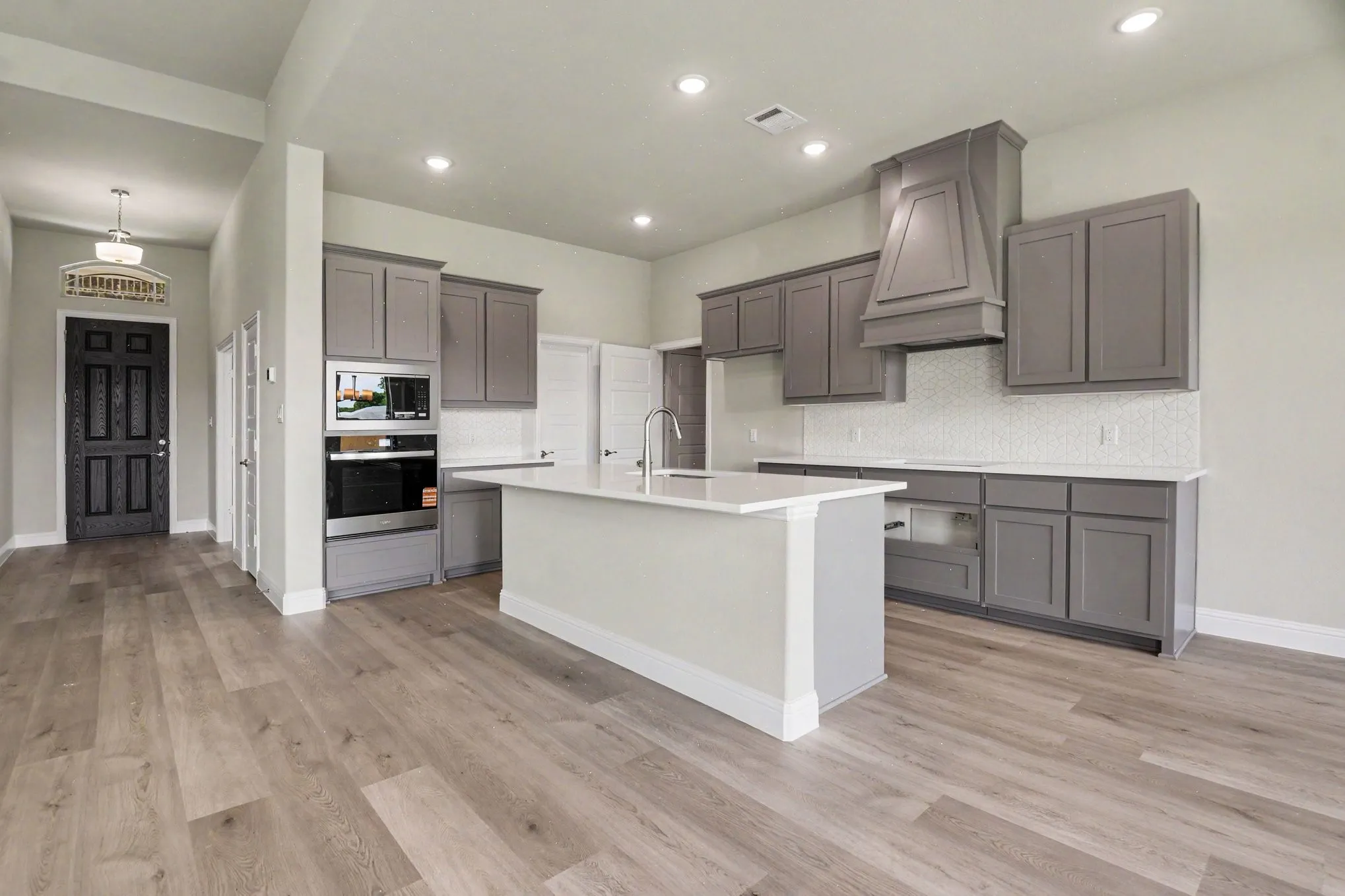 Contemporary kitchen featuring a central island, light gray cabinetry, built-in stainless steel appliances, a decorative range hood, and wood-finish flooring