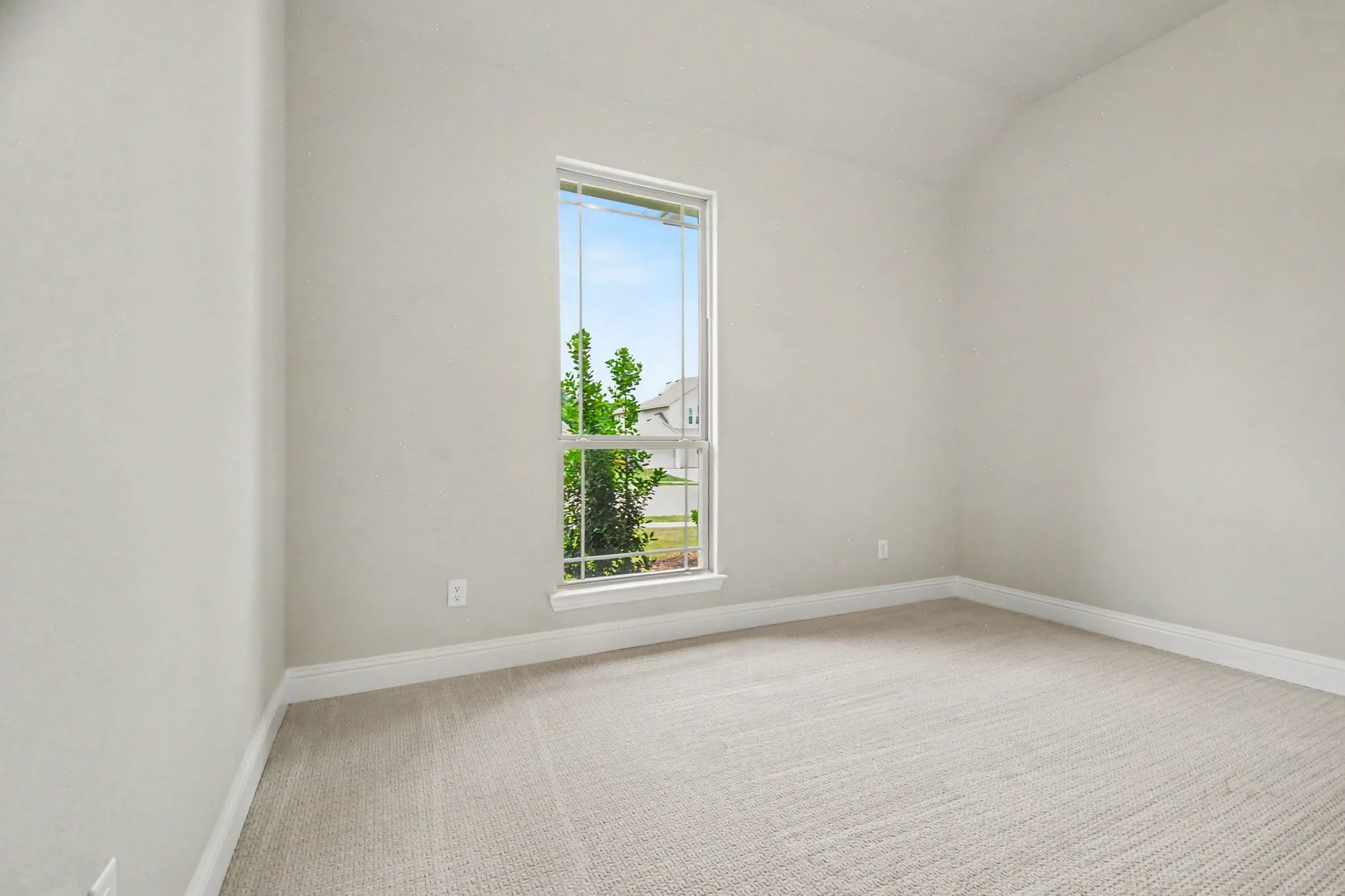 Bright interior room featuring a large window, neutral wall paint, light-toned carpeting, and a vaulted ceiling