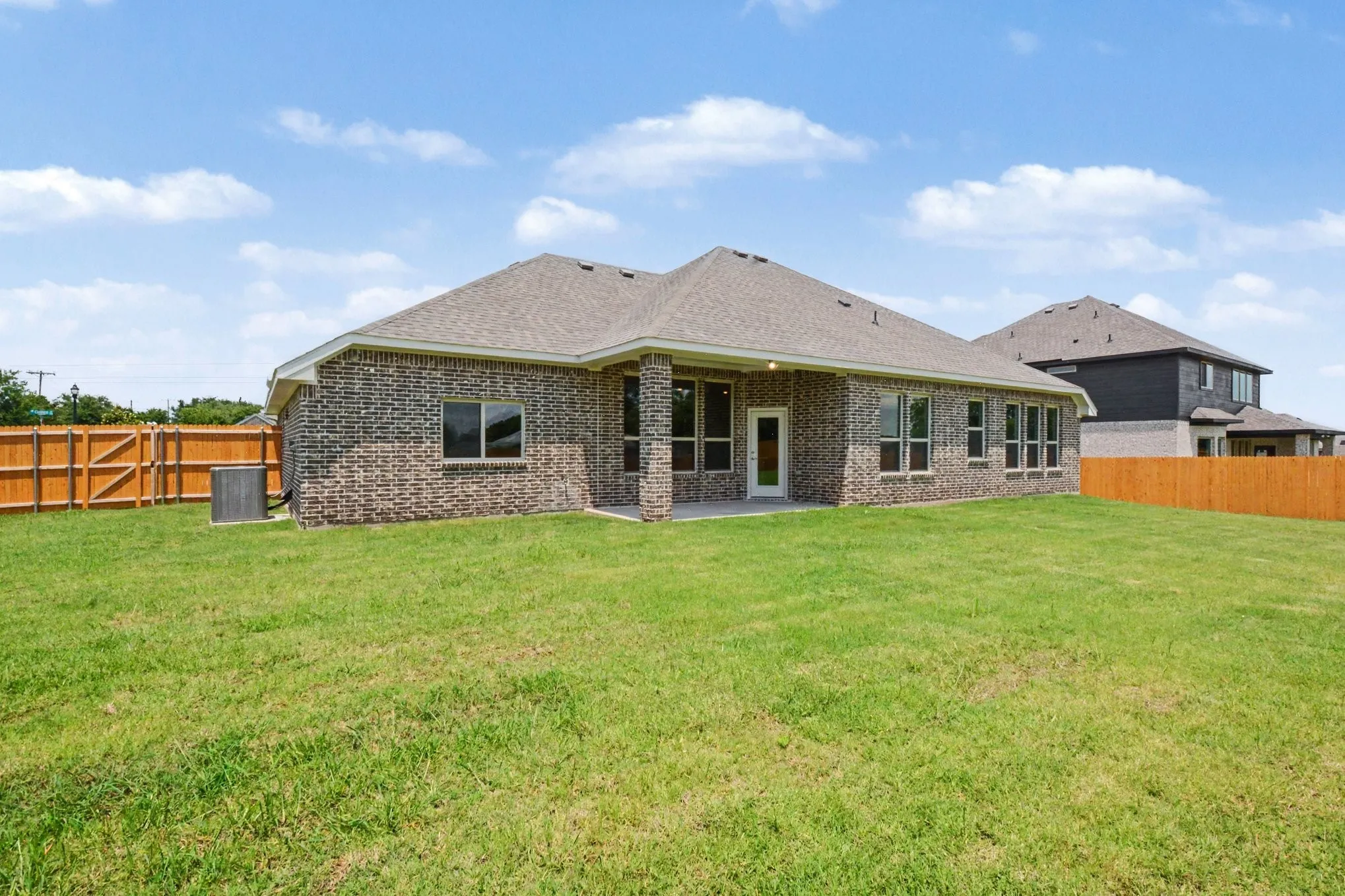 Expansive backyard featuring a manicured lawn, full privacy fencing, a covered concrete patio, and a brick exterior with multiple windows