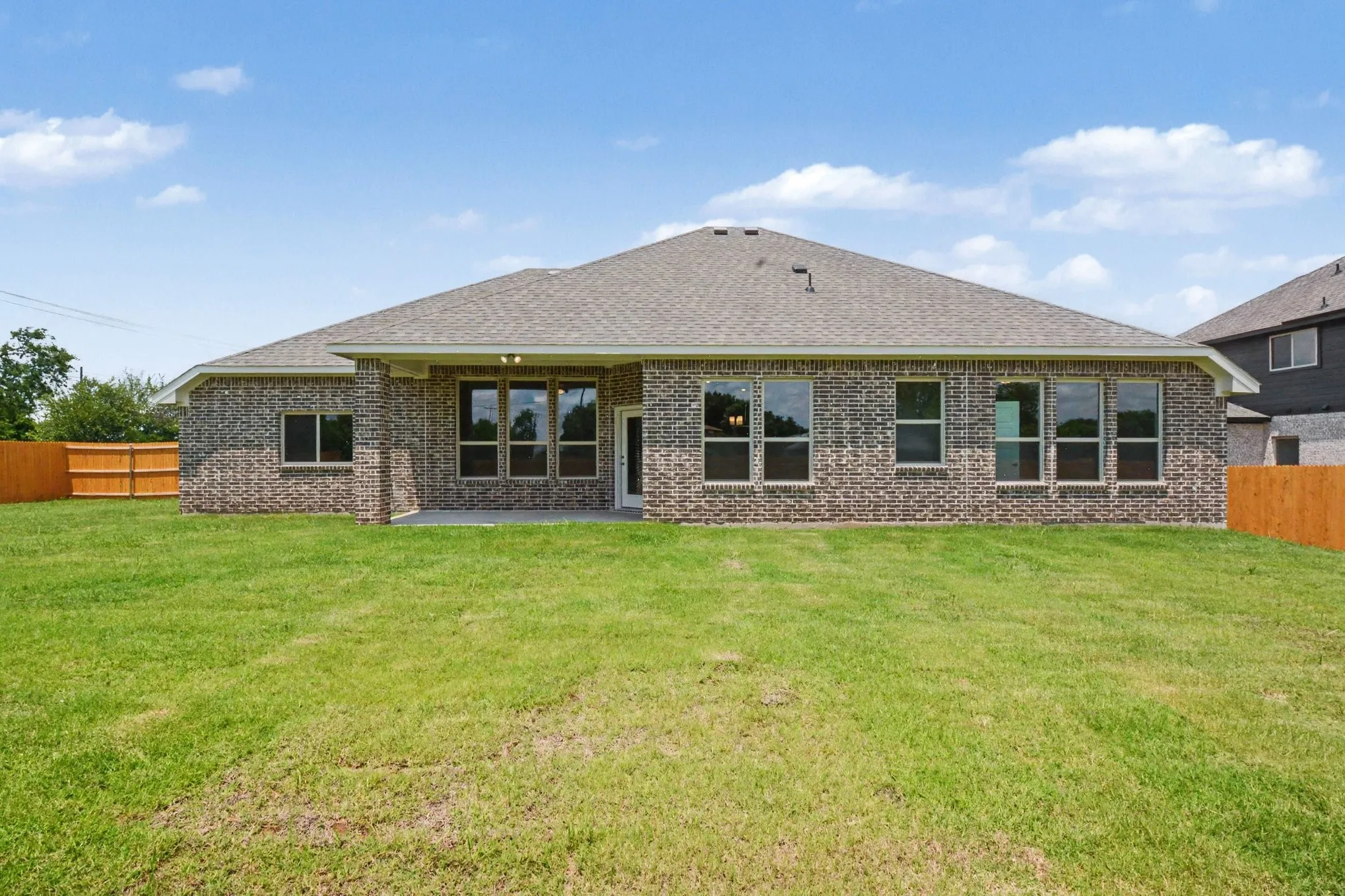 Expansive backyard featuring a manicured lawn, full brick exterior, a covered patio, and privacy fencing