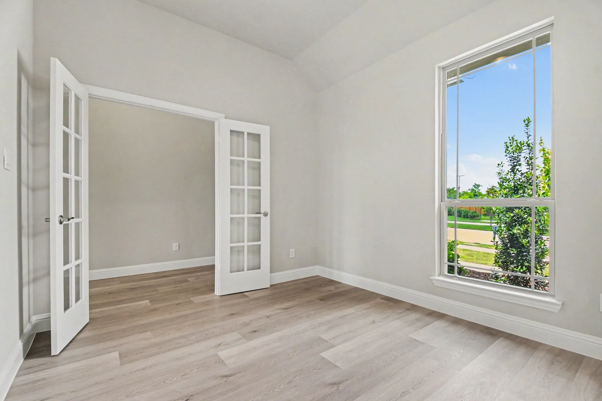 Room featuring French doors with glass panes, wood-finish flooring, a tall window, and white baseboards